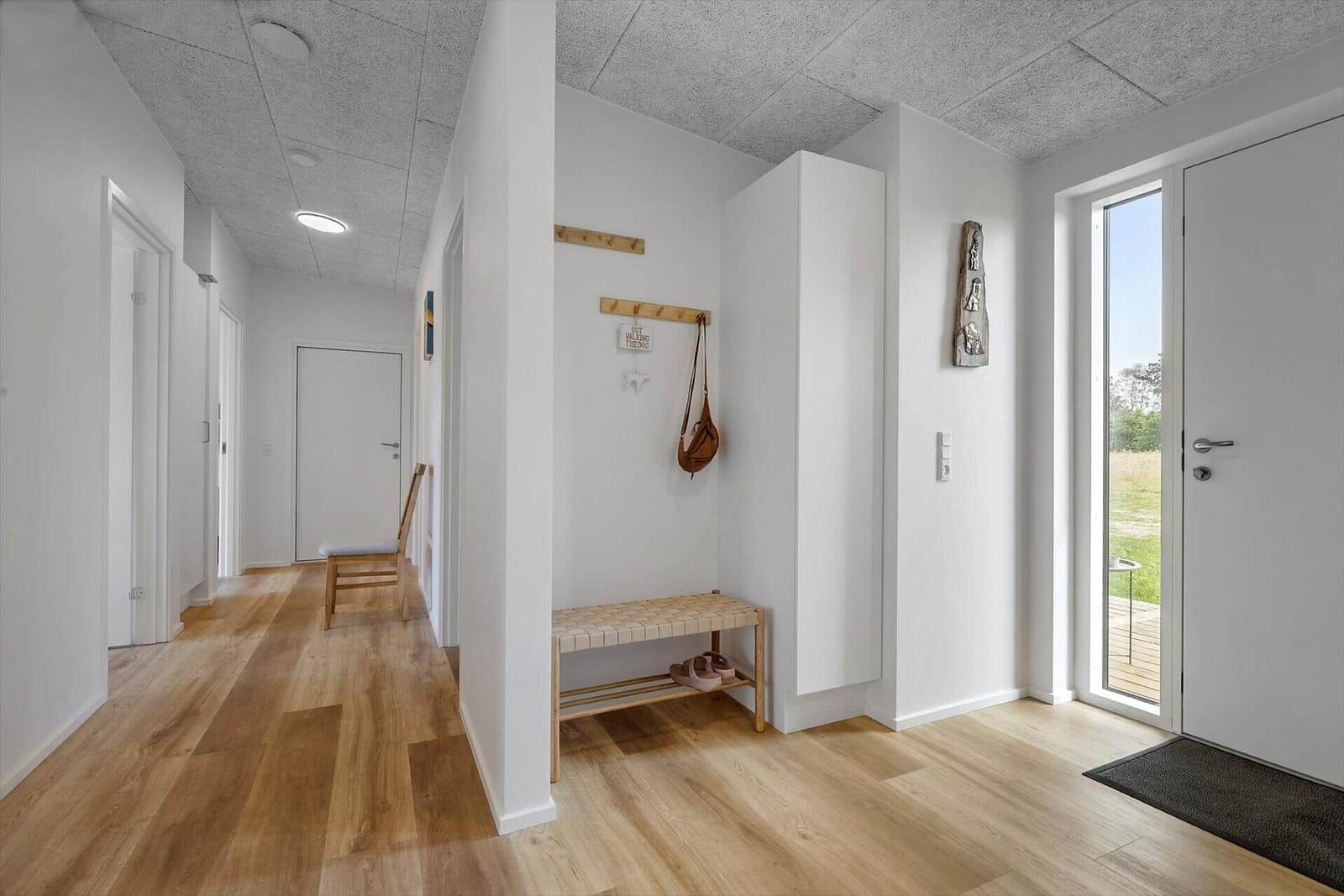 Hausflur mit Holzboden, Kleiderhaken und Sitzbank. Tür führt nach draußen.