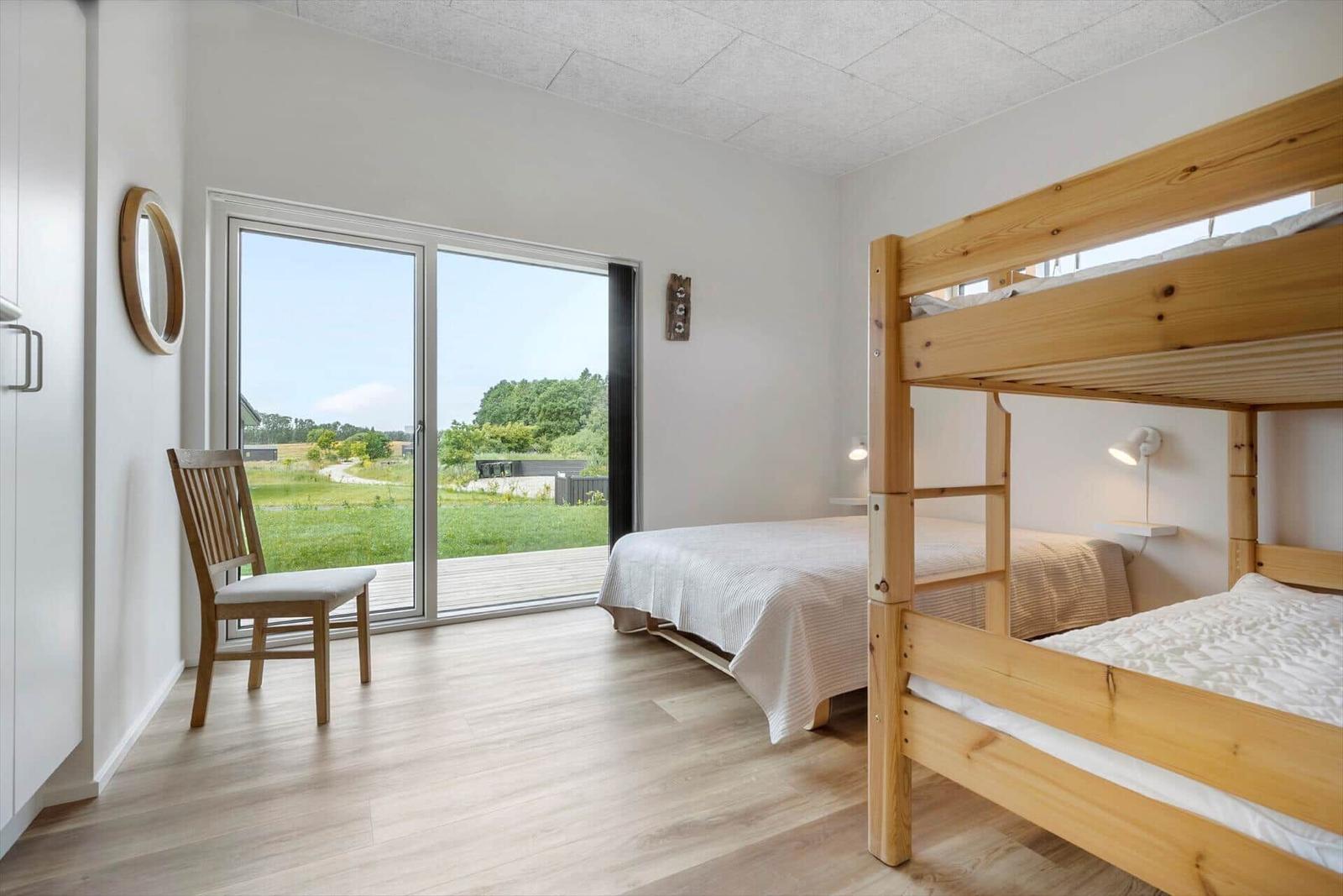 Zimmer mit Doppelbett und Schlafcouch, großes Fenster mit Blick auf Grünflächen.