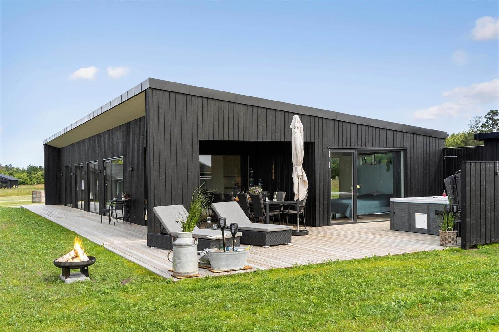 Moderne Villa mit Terrasse, Liegen, Grill und Whirlpool. Grünfläche und klarer Himmel.