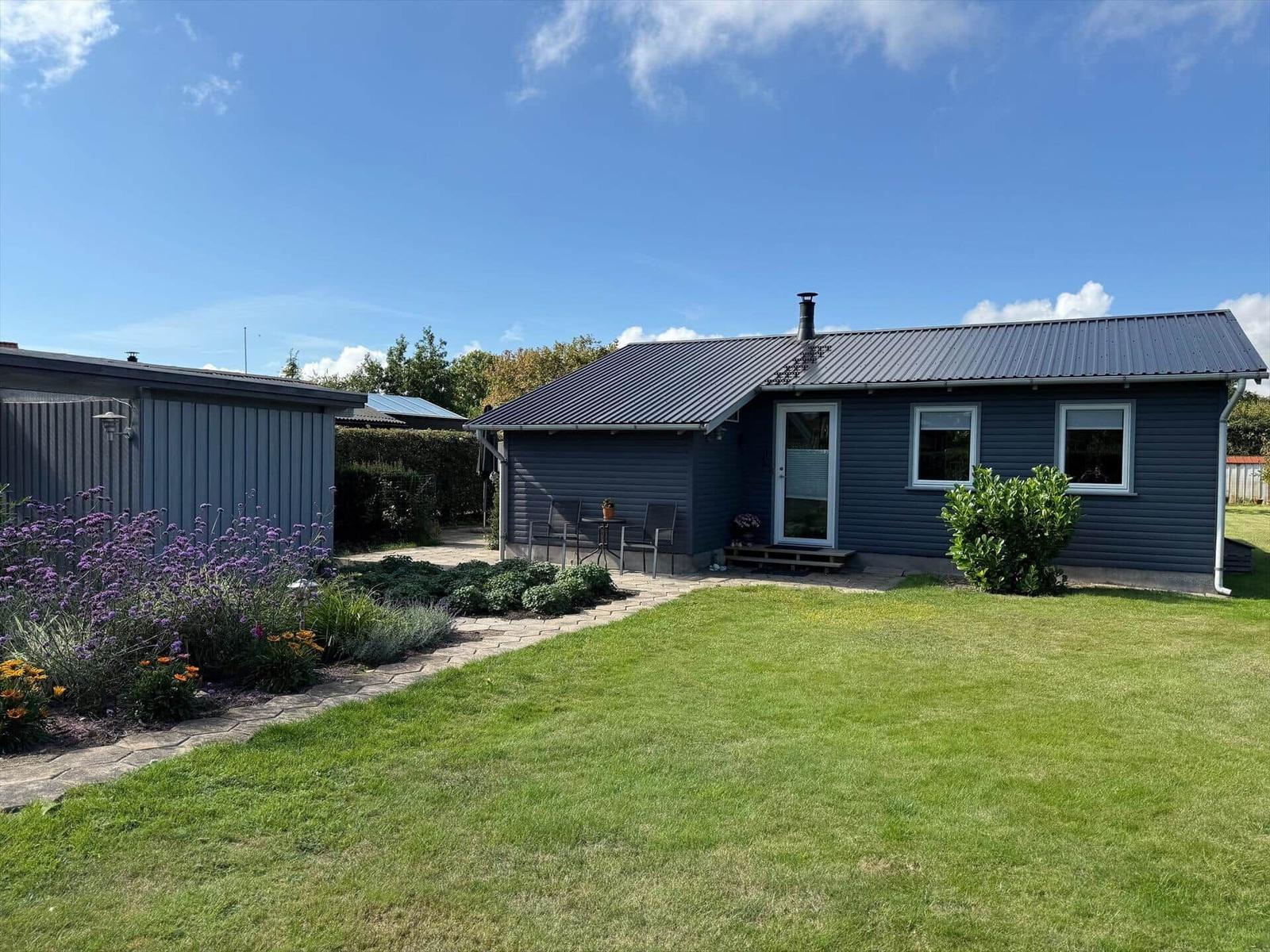 Ein Haus mit Garten, Terrasse und Blumenbeet unter blauem Himmel.