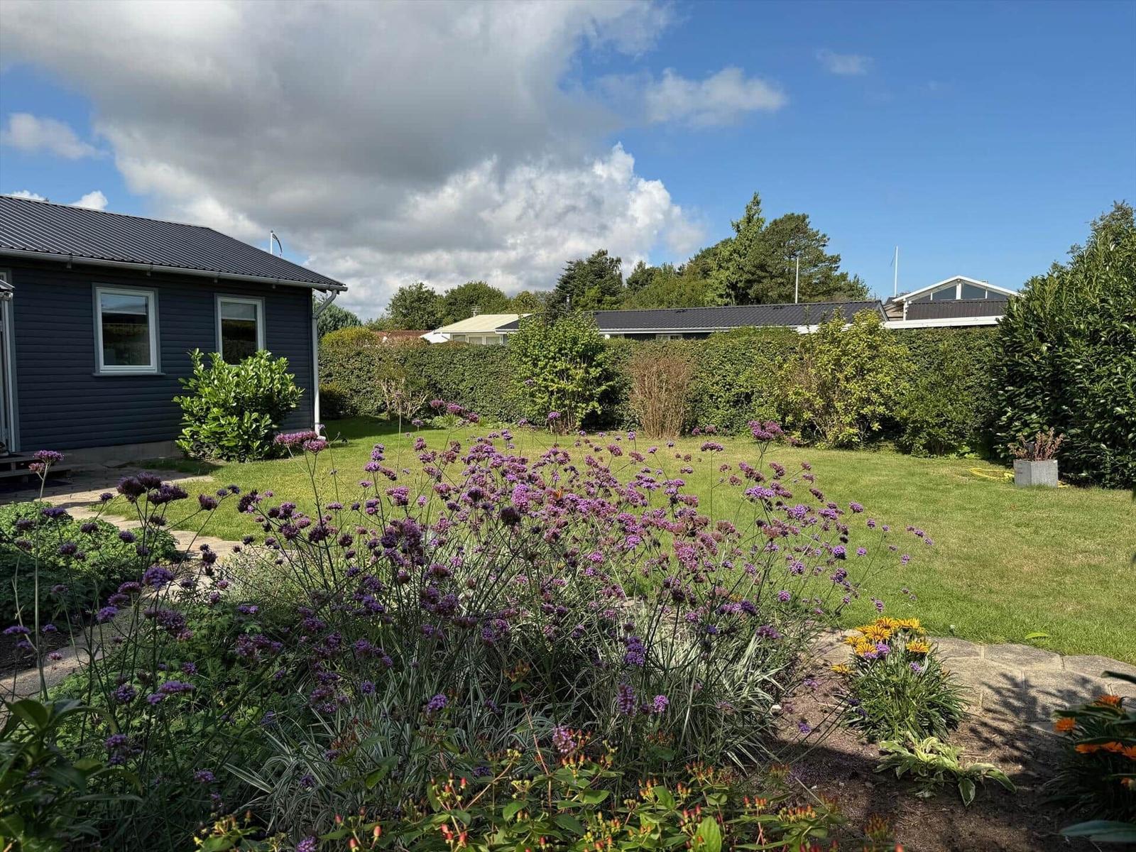 Garten mit blühenden Pflanzen und einem Haus im Hintergrund.