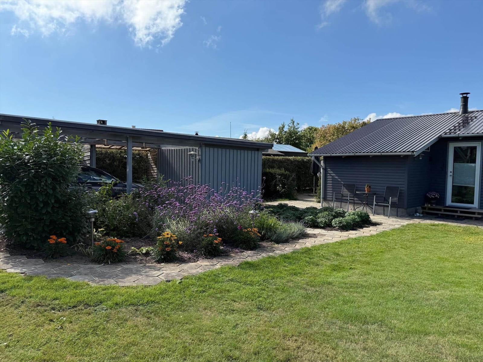Haus mit Garten, Terrasse und Blumenbeeten unter blauem Himmel.