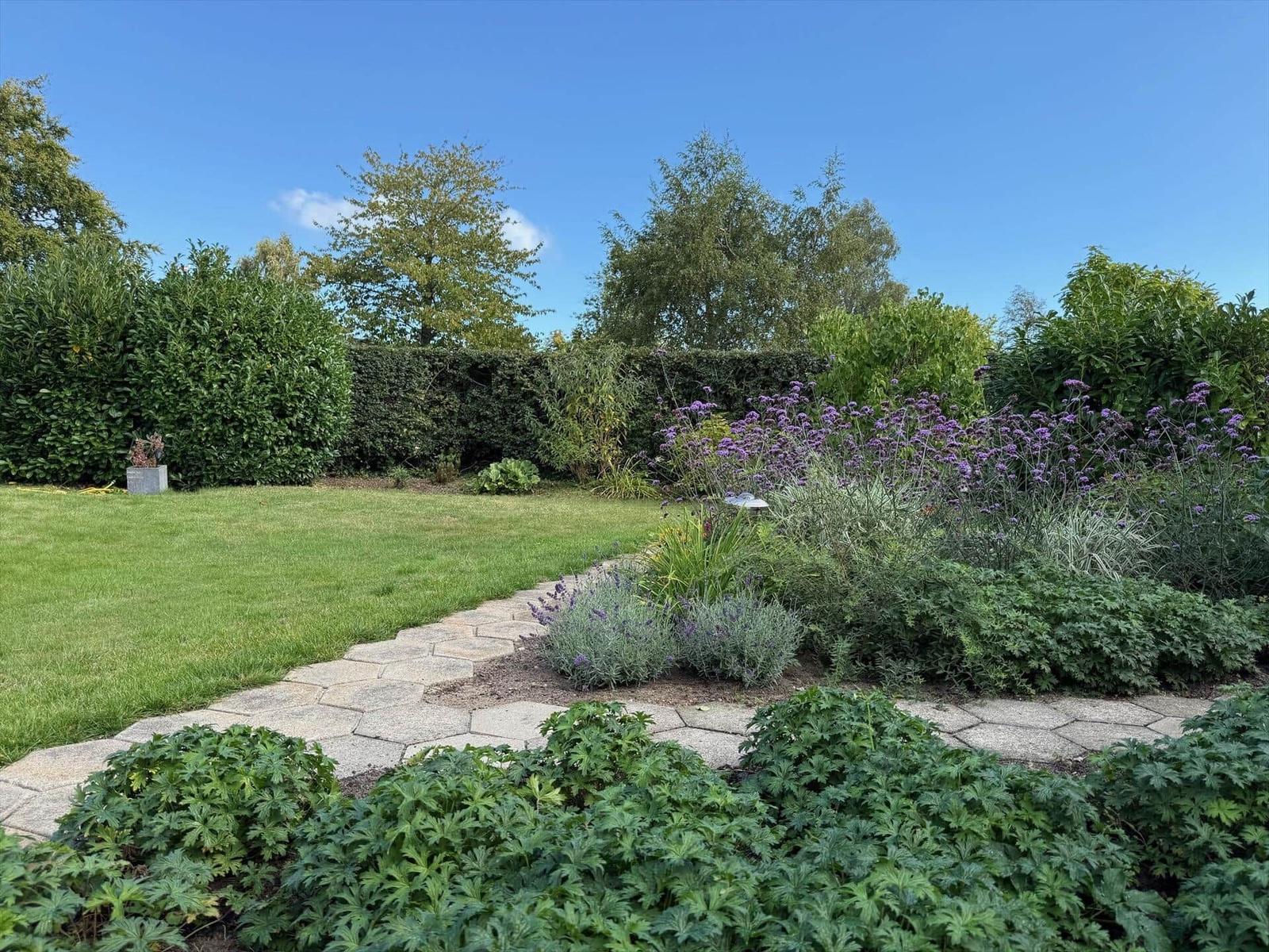 Garten mit gepflastertem Weg, Grasfläche und blühenden Pflanzen.