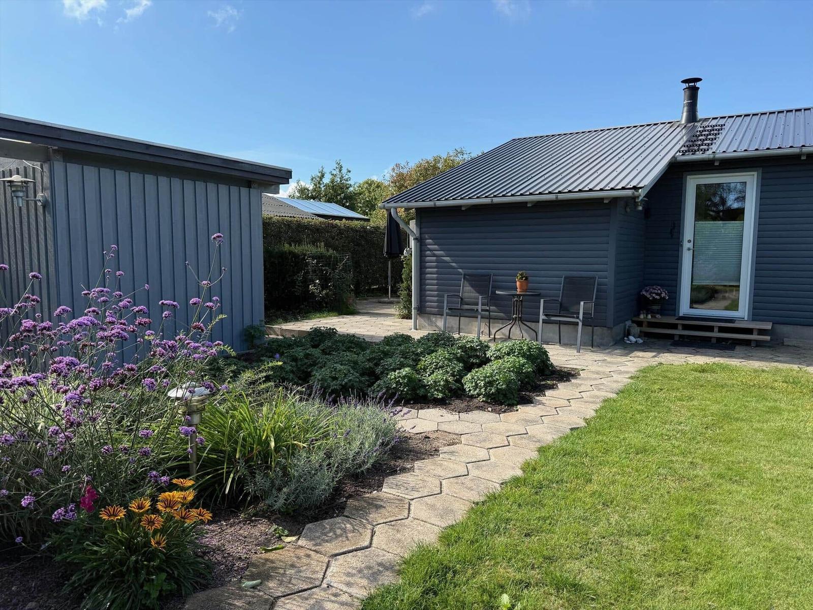 Haus mit Garten, Terrasse und Sitzgelegenheit unter blauem Himmel.