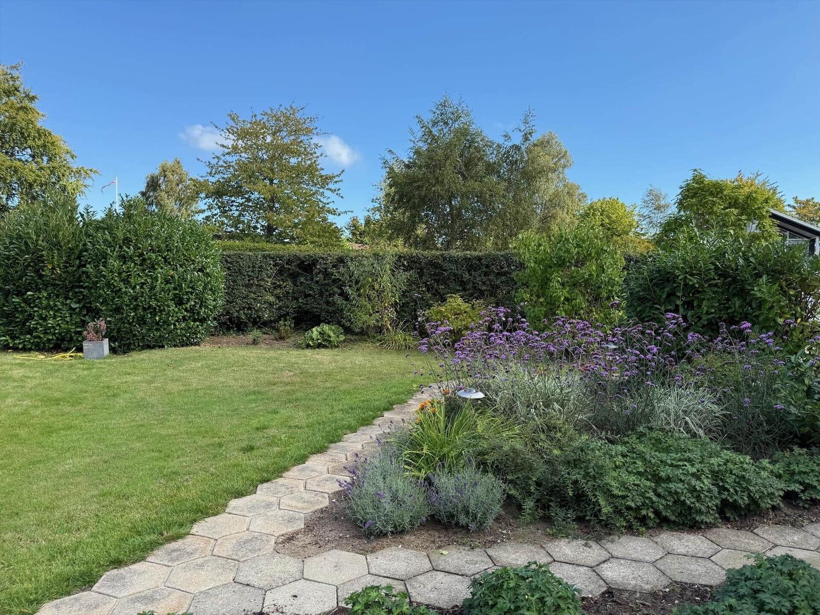 Garten mit Rasen, Hexagon-Pflasterweg und blühenden Pflanzen.