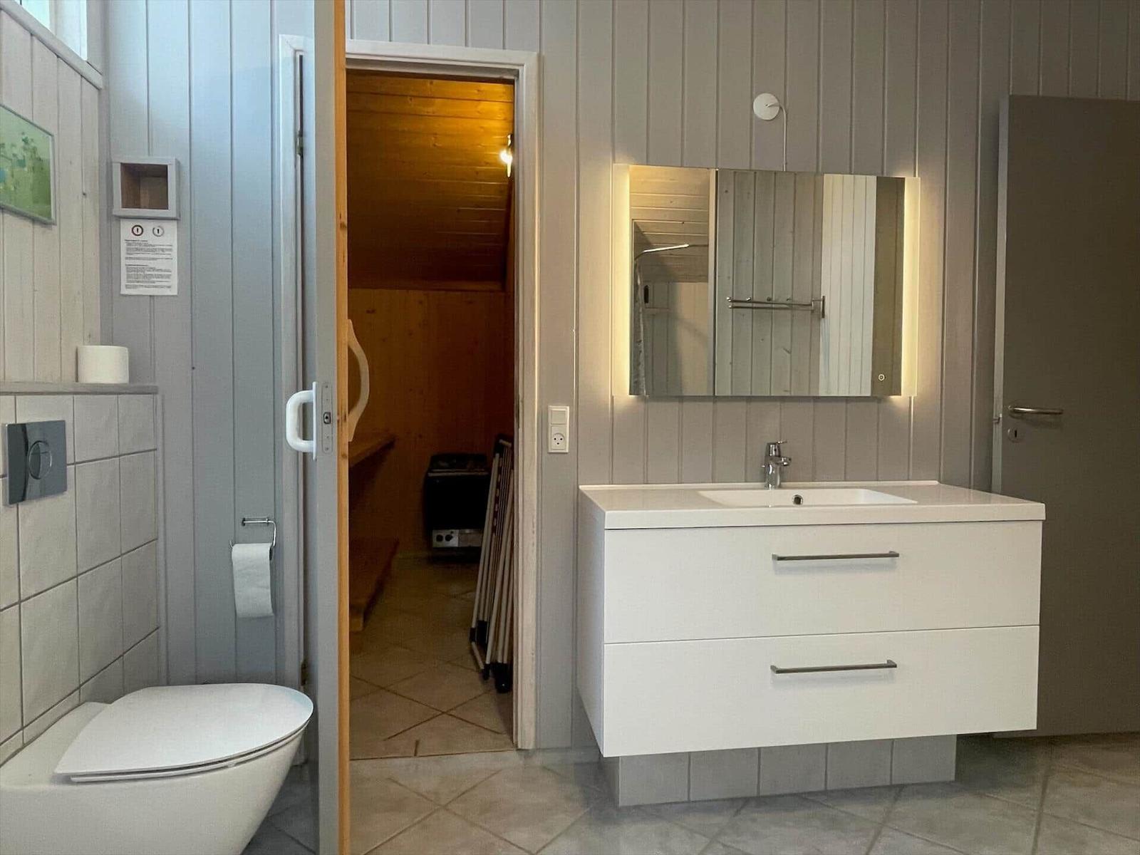 Bad mit Waschbecken, Spiegel und Toilette. Durchgang zur Sauna.