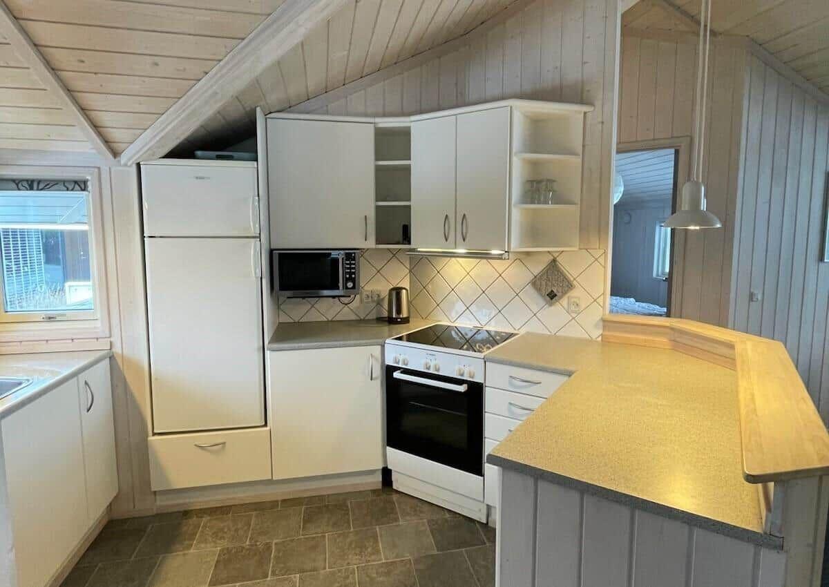 Küche mit weißen Schränken, Kühlschrank, Mikrowelle und Herd.