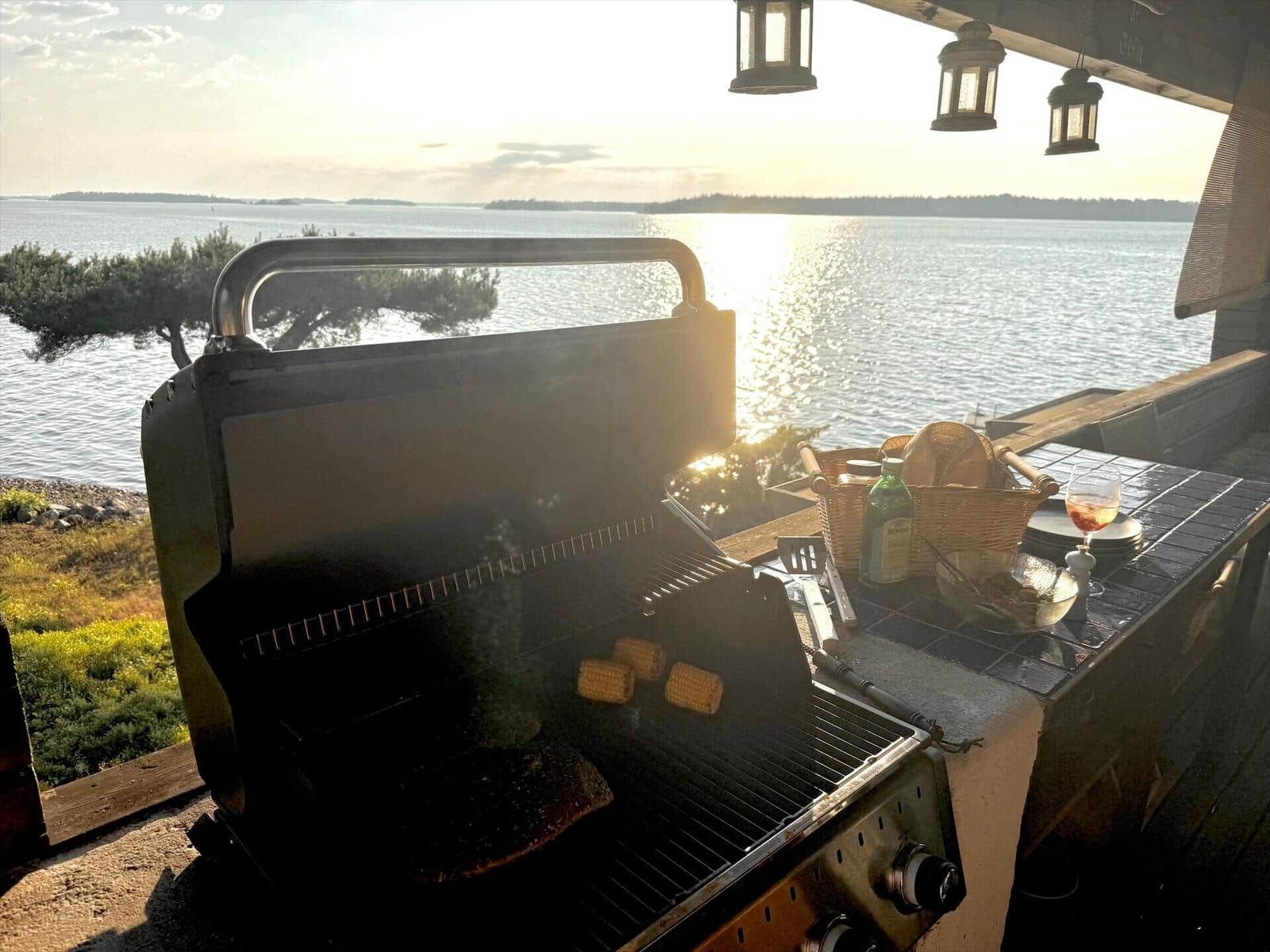 Grill mit Mais und Fisch auf Terrasse mit Blick auf See.