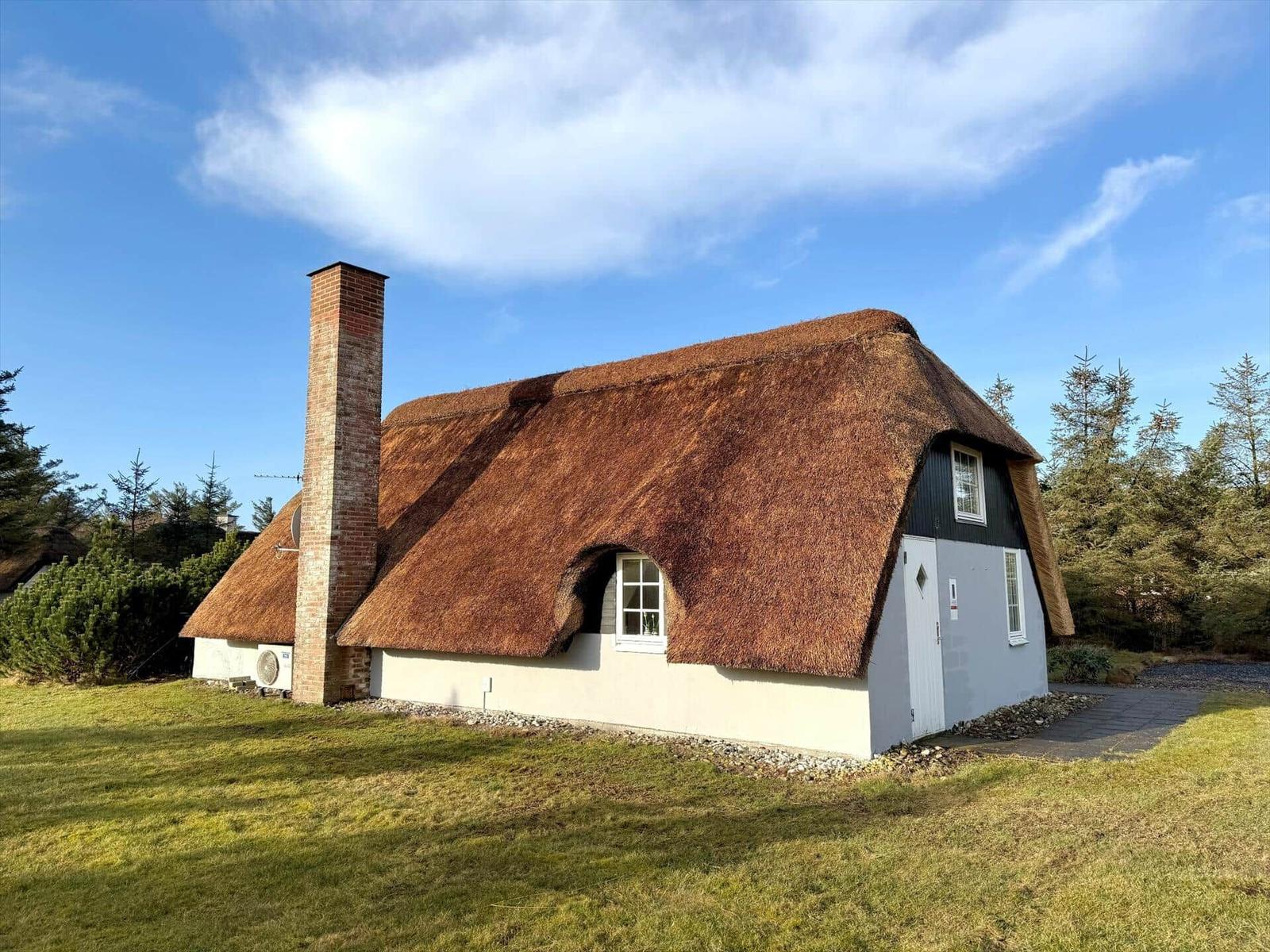 Haus mit strohgedecktem Dach, Backstein-Schornstein und weißer Fassade.
