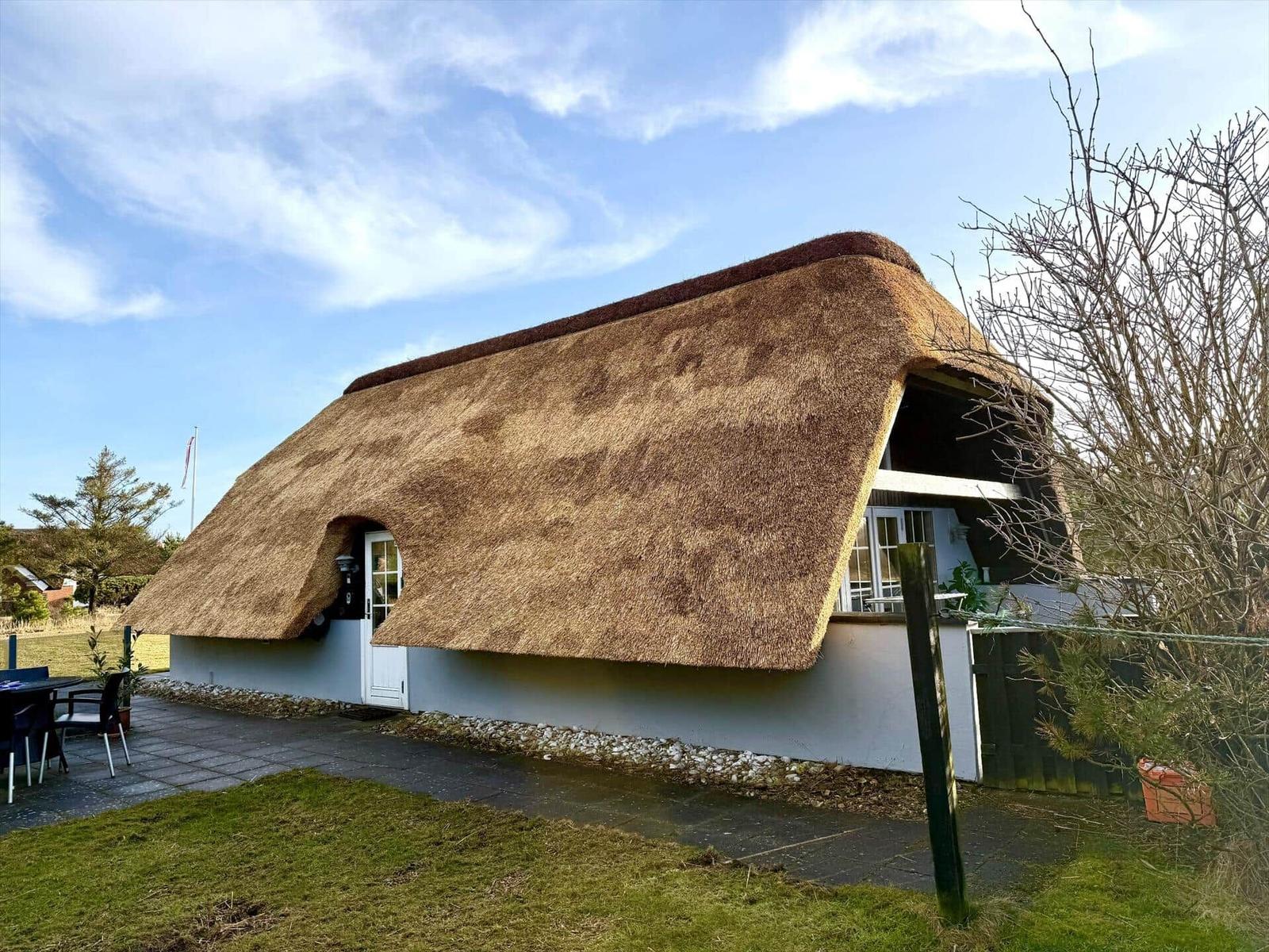 Haus mit Strohdach, weißer Wand und Terrasse im Freien.