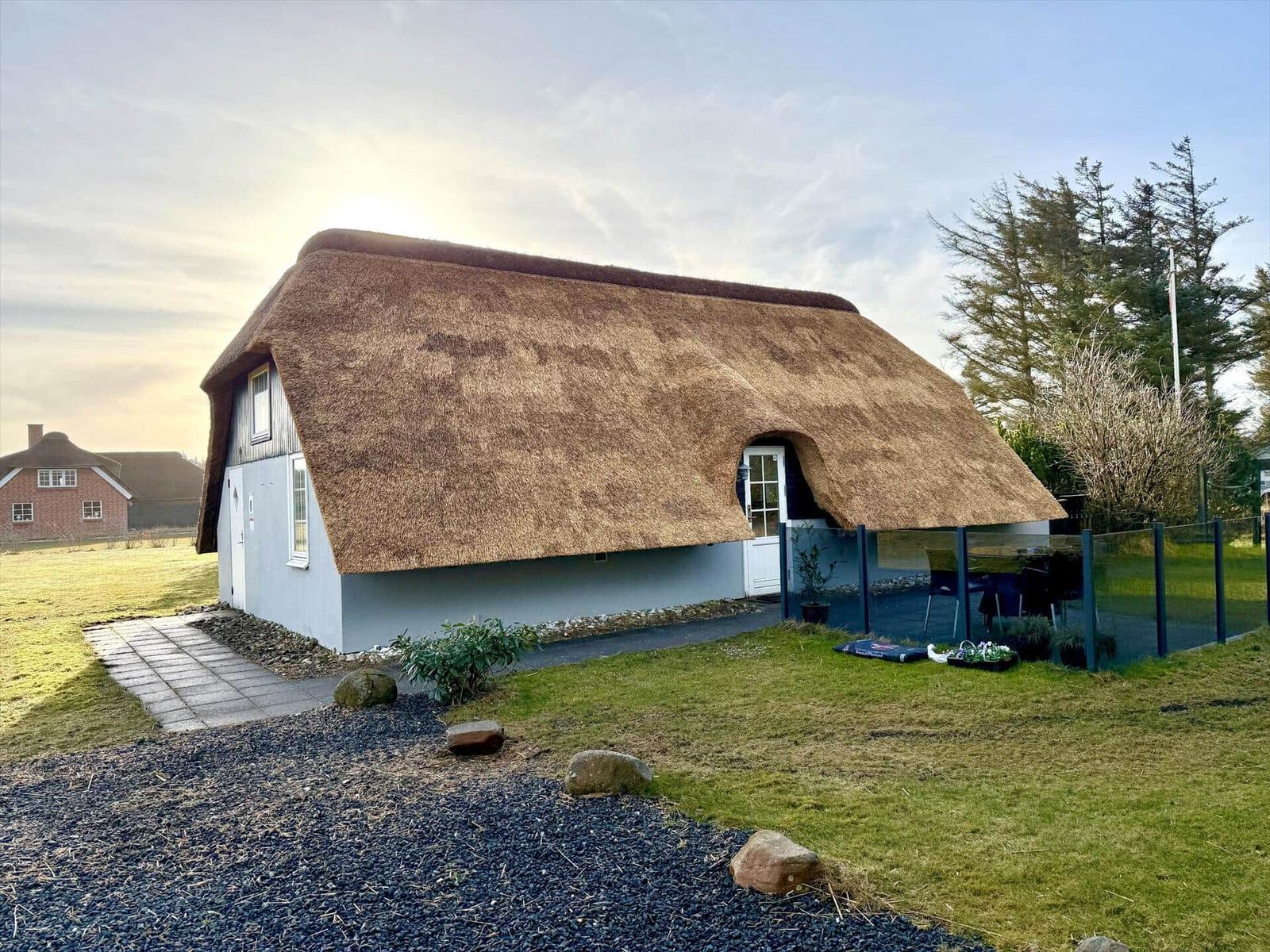Haus mit Strohdach, Garten und Terrasse mit Sitzgelegenheit.