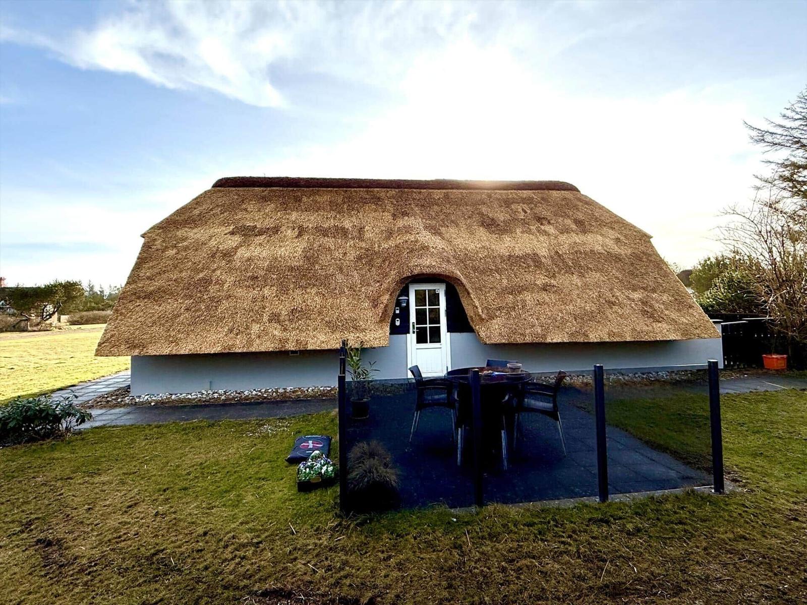 Haus mit Strohdach, Terrasse und Garten. Weiße Tür und schwarze Möbel.