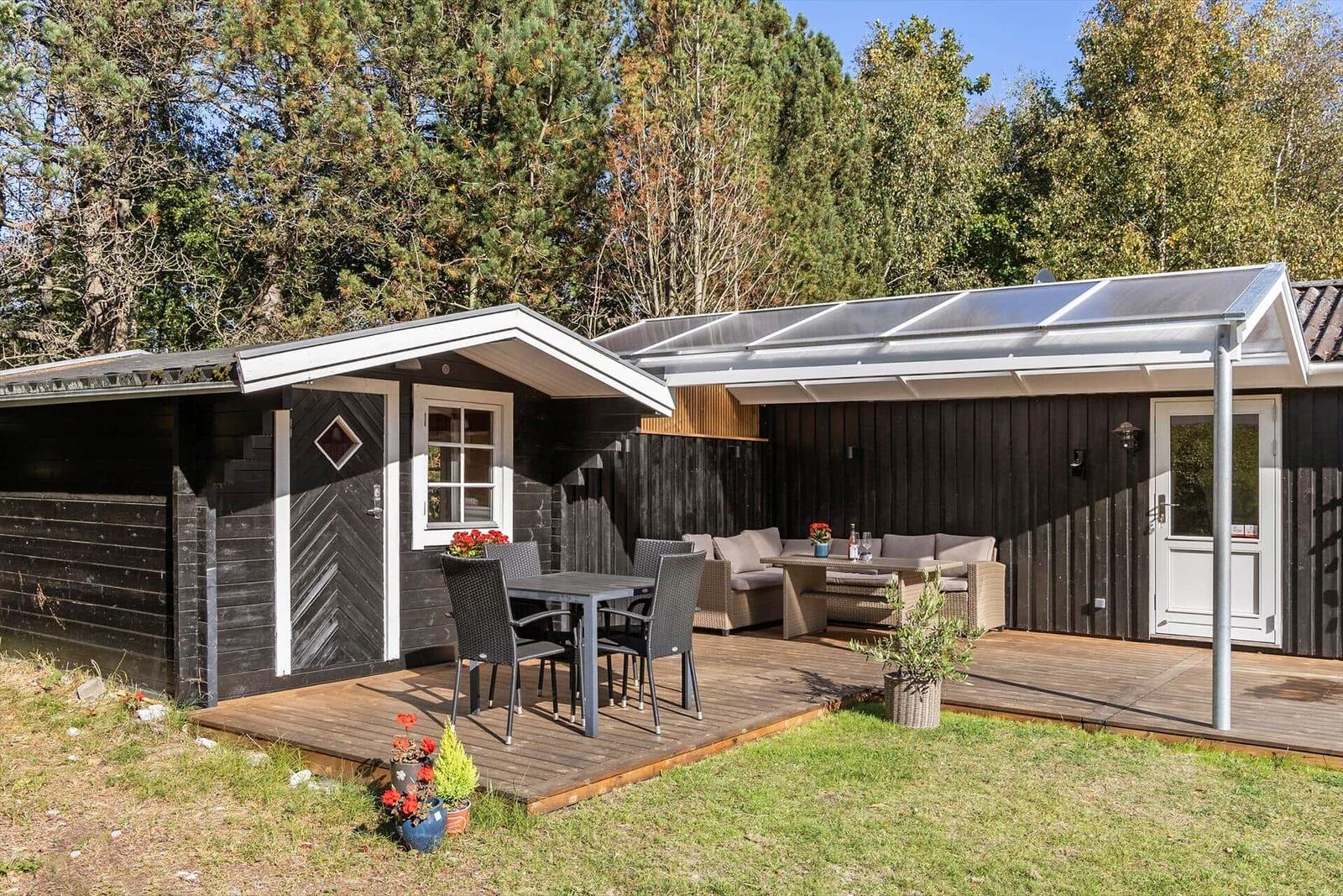 Holzhaus mit Terrasse, Sitzgruppe und Tisch. Umgeben von Bäumen.