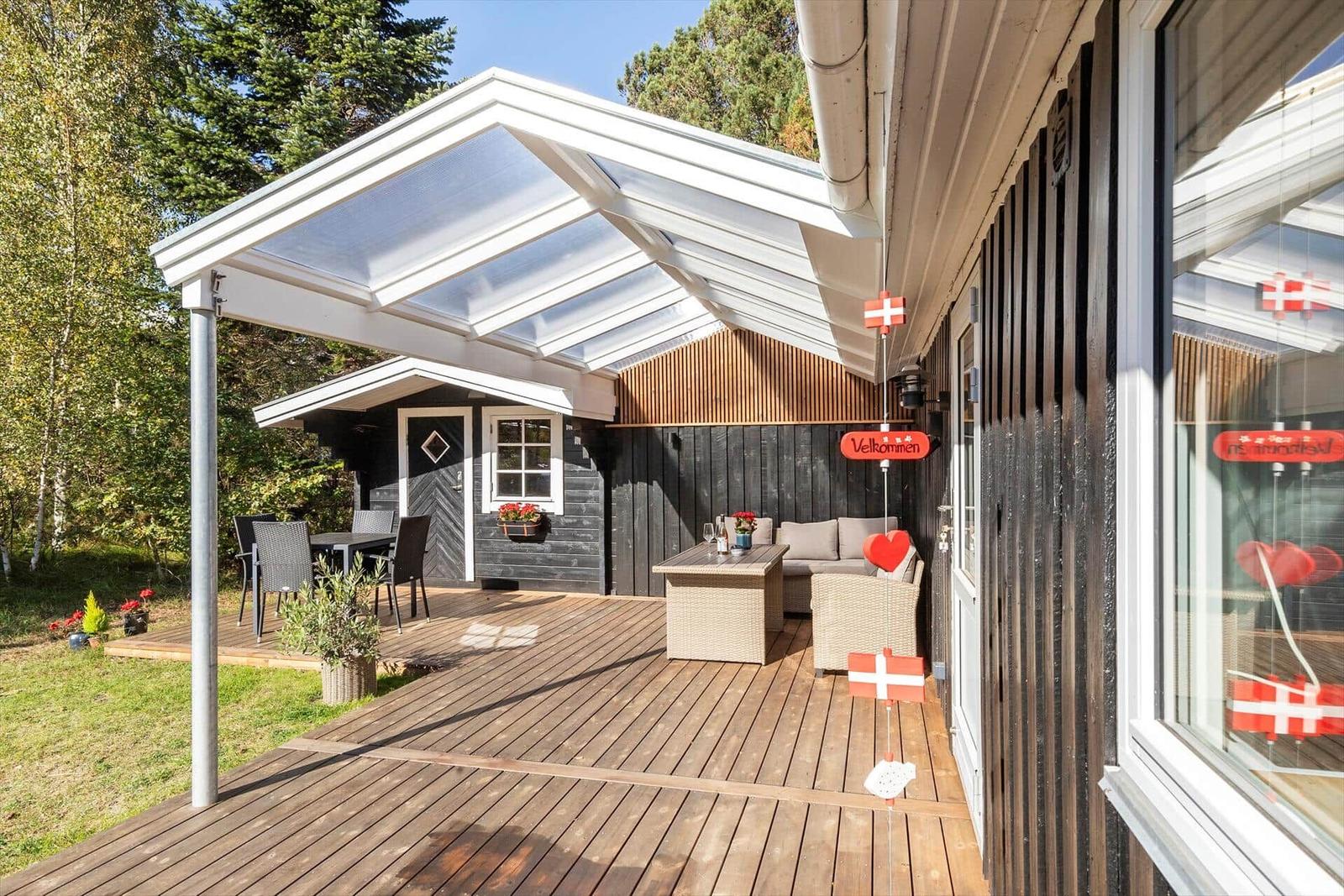 Terrasse mit Sitzgelegenheiten und transparentem Dach. Holzdecke, Pflanzen und dänische Flaggen.