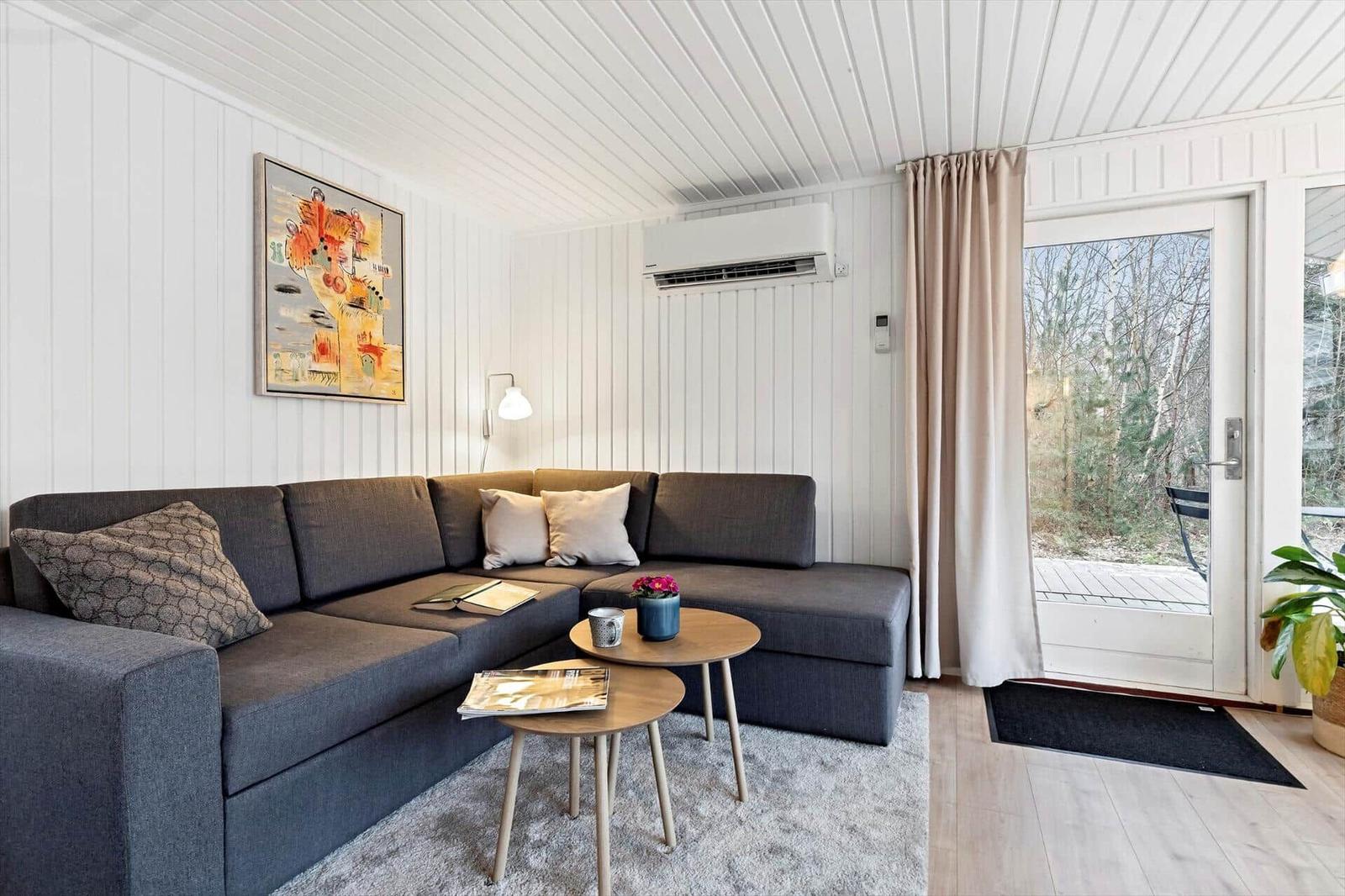 Ein Wohnzimmer mit grauem Sofa, zwei runden Tischen und einer Glastür zum Balkon.