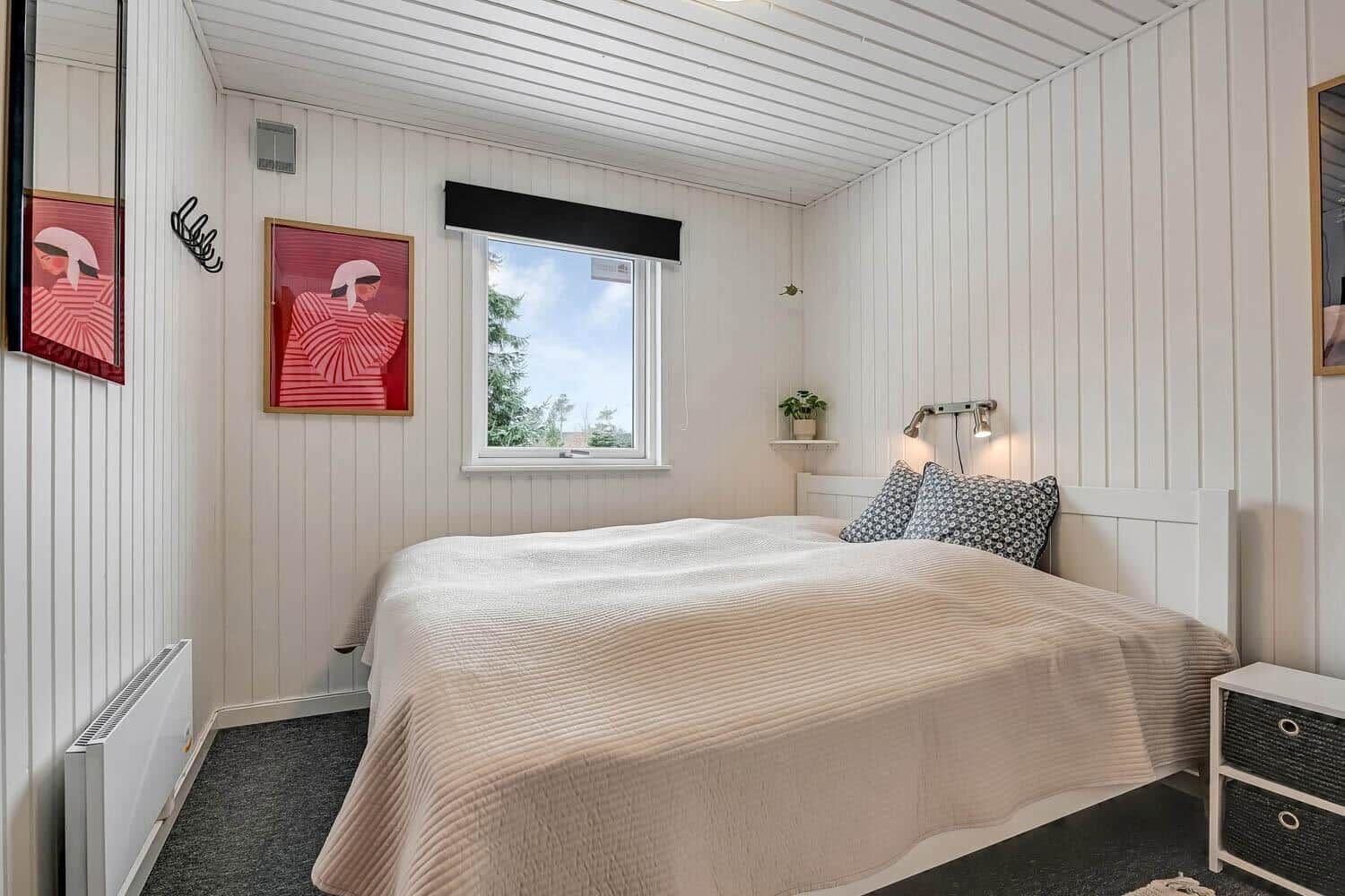 Schlafzimmer mit Bett, Fenster und Wandbildern.