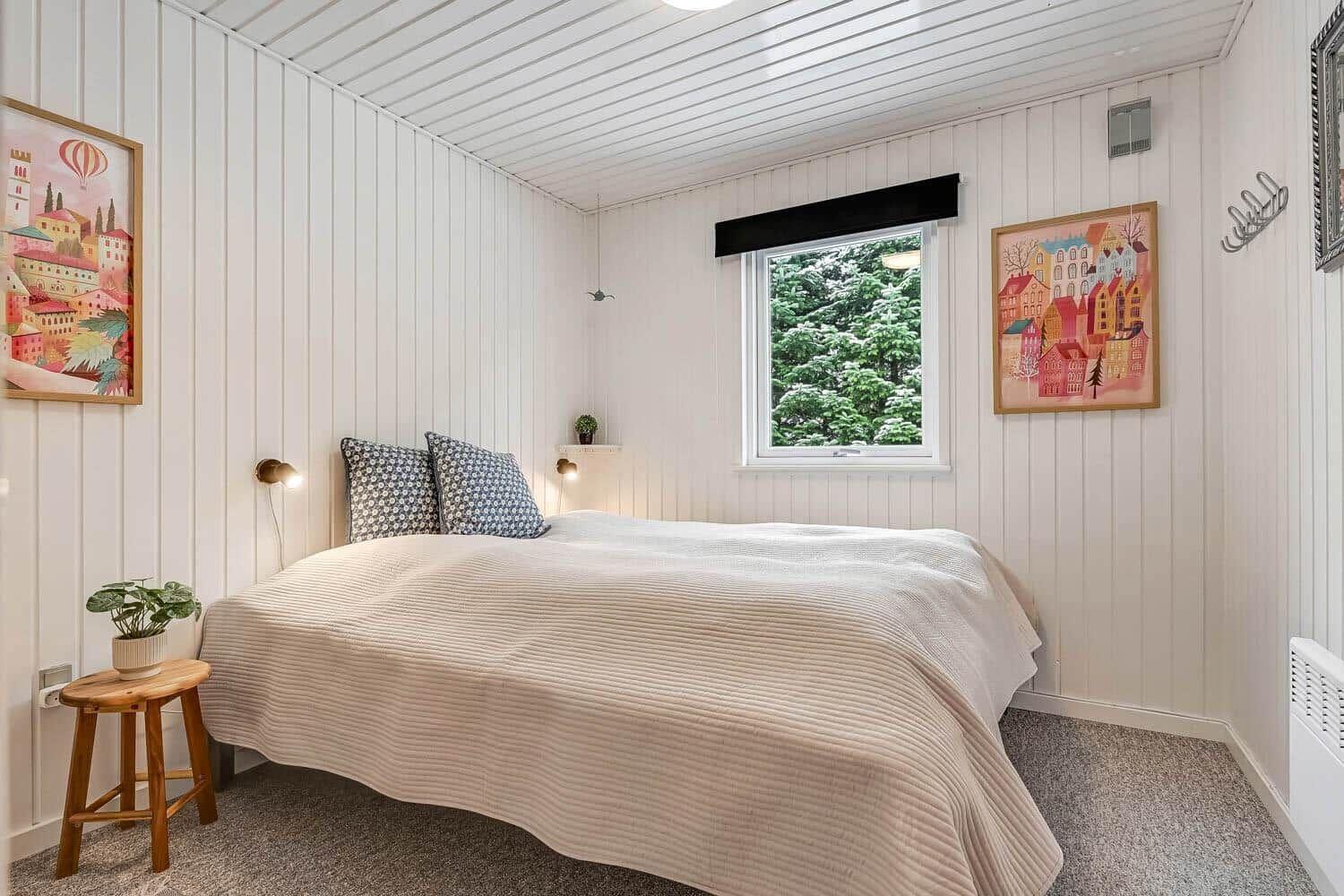 Schlafzimmer mit Bett, Fenster und Wandbildern.