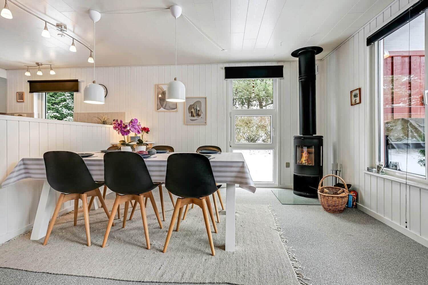Esszimmer mit Esstisch, Stühlen und Kaminofen. Große Fenster und helle Wände.