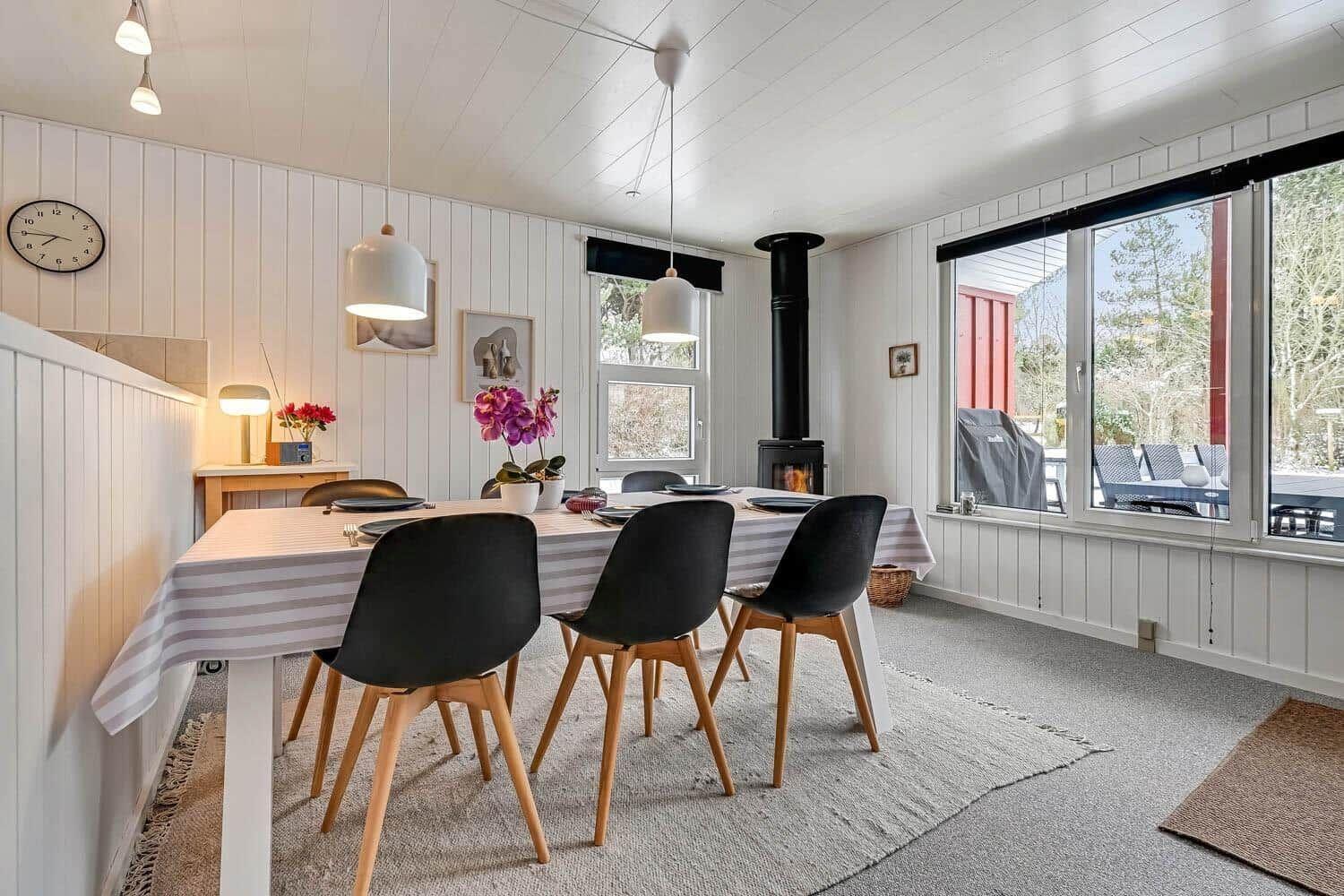 Esszimmer mit Tisch, Stühlen und Kamin. Große Fenster bieten Blick auf Außenbereich.