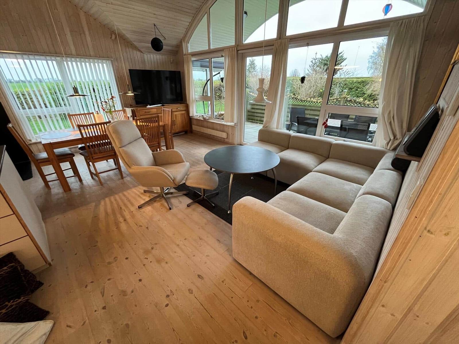 Wohn- und Essbereich mit Sofa, Sessel und TV. Holzboden und große Fenster.