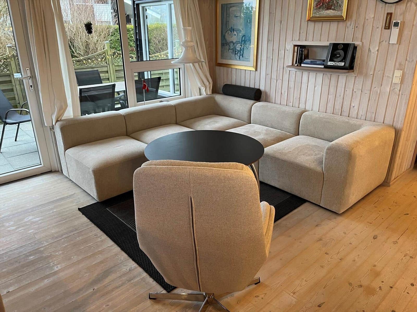 Wohnzimmer mit Ecksofa, runden Tisch und Stuhl. Holzwand und Terrassentür.