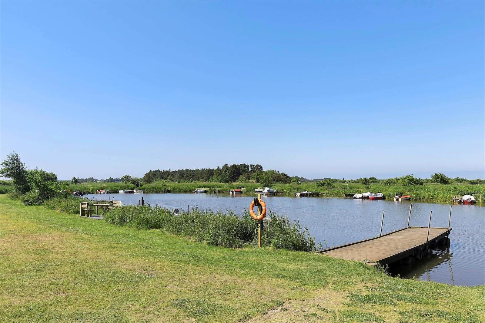 Holzsteg führt zu einem See mit Booten und Grünflächen.