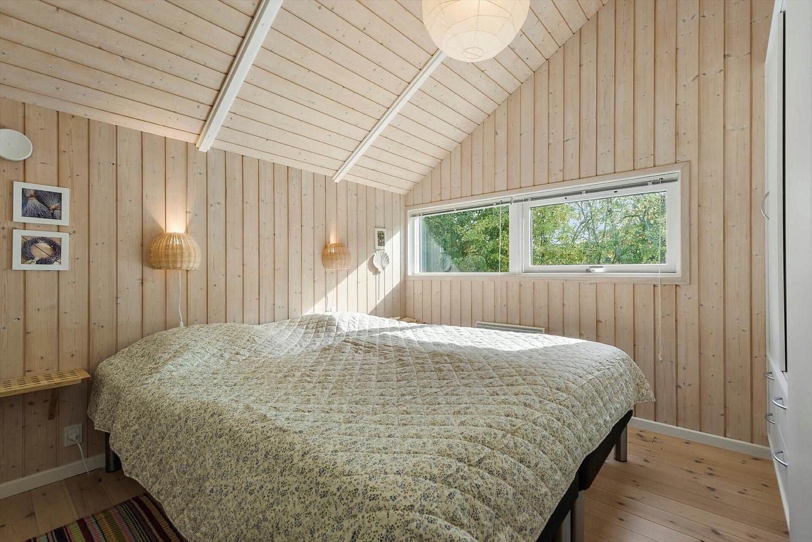 Bedroom with wooden walls, bed, and window to the garden.