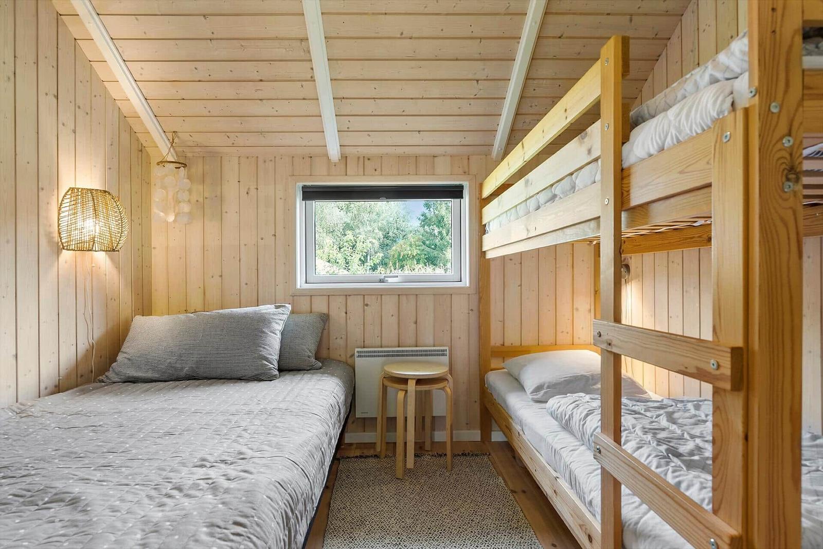 Room with wooden walls, bunk bed, and window with view of trees.