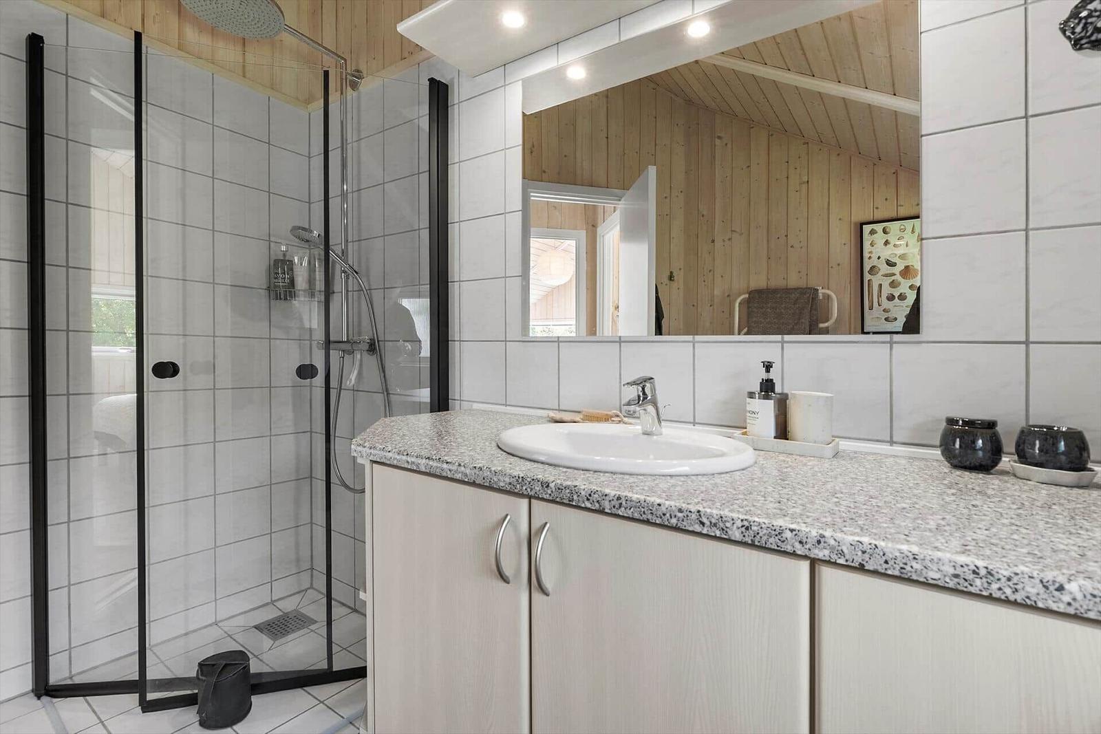 Bathroom with shower, sink, and mirror. Wooden walls and tiles.