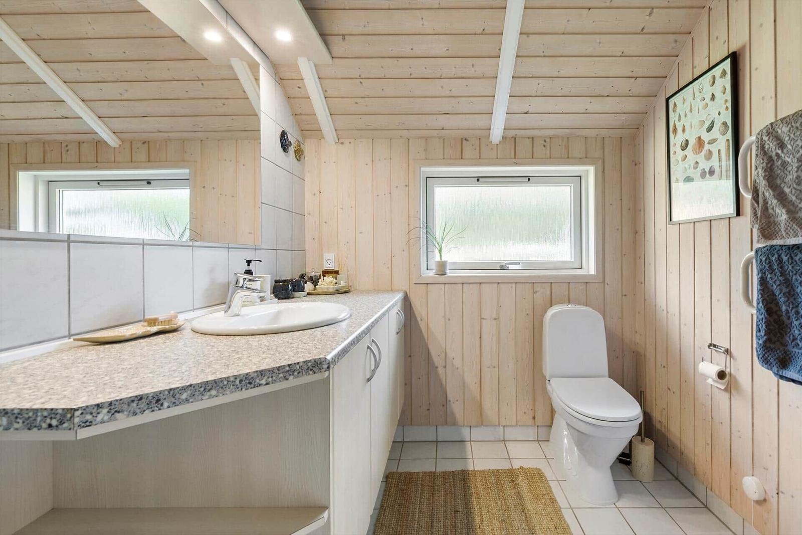Bathroom with sink, toilet, and window. Wooden walls and floor tiles.