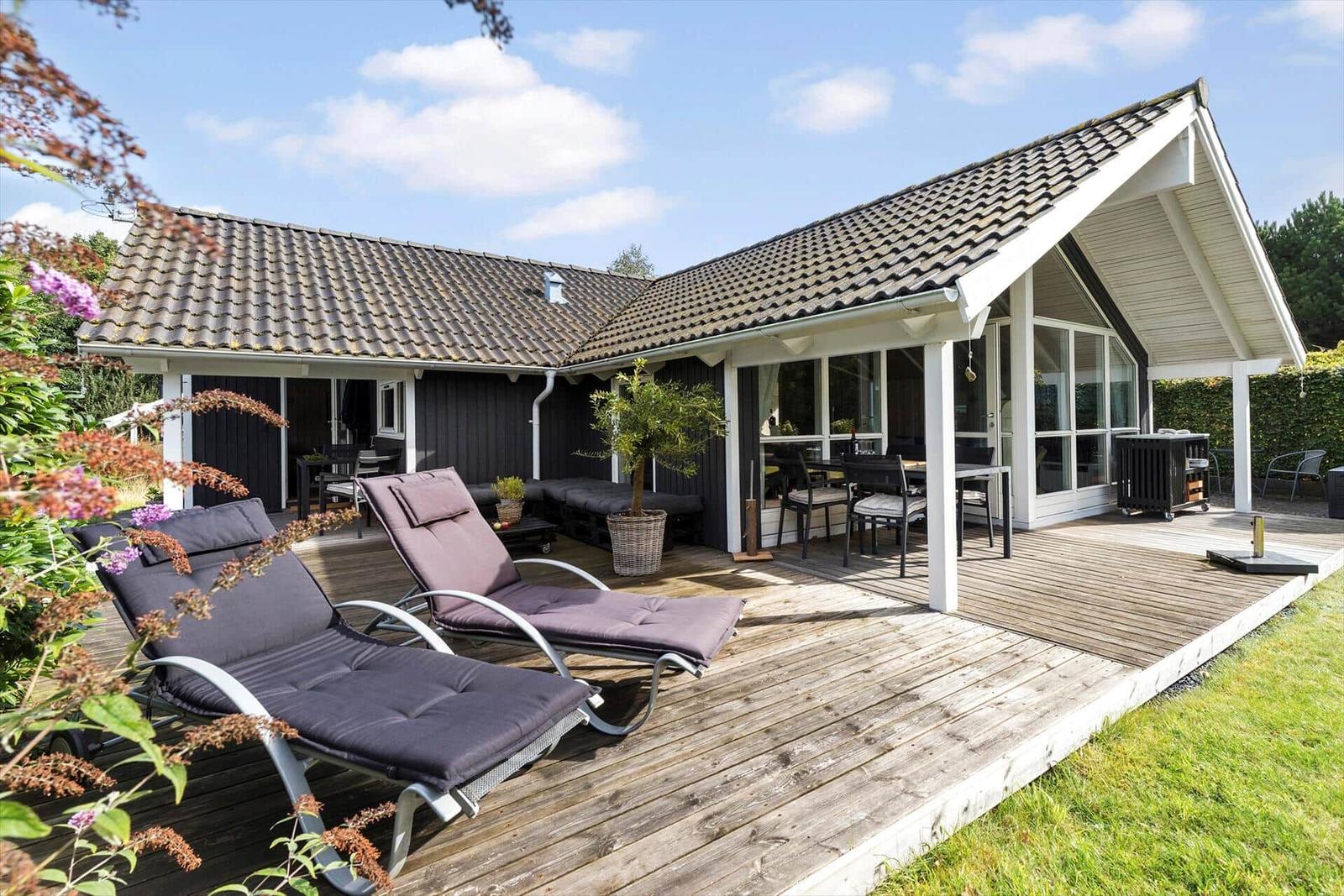 Deck with loungers, table and chairs. House with roof and glass front.