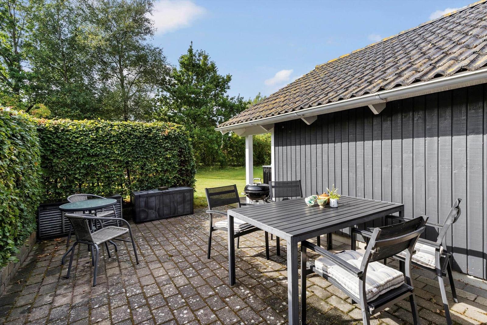 Terrace with table, chairs, grill, and planters. Backyard with hedge and lawn.