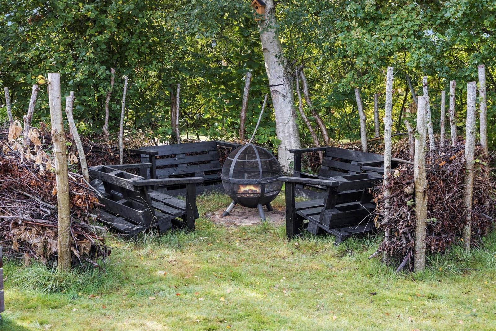 Fire pit with seating in the garden. Surrounded by trees and hedges.