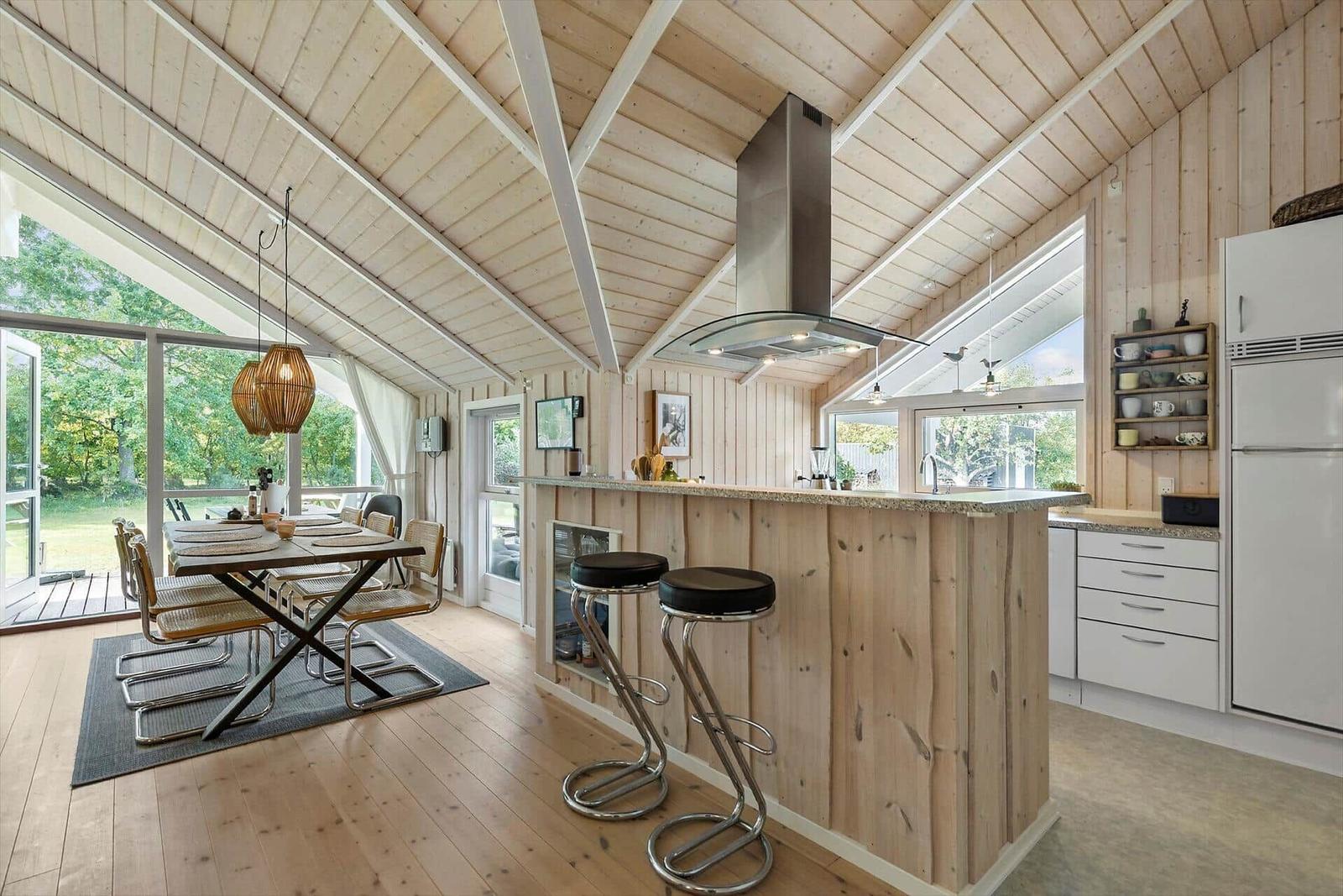 Kitchen with dining area, wood walls and ceiling, bar stools, and windows to the outside.