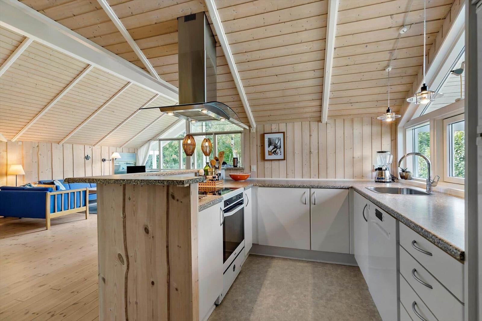Kitchen with wooden ceiling, white cabinets, and kitchen island. Living area with blue sofa in background.