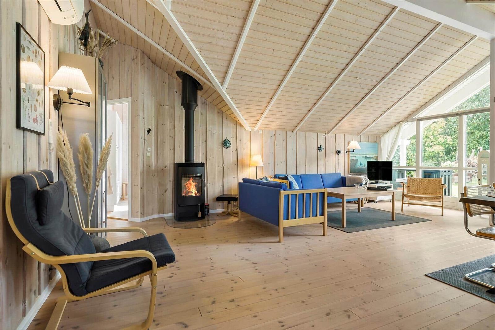 Living room with wood walls, fireplace, and blue sofa. Wooden floor and large windows.