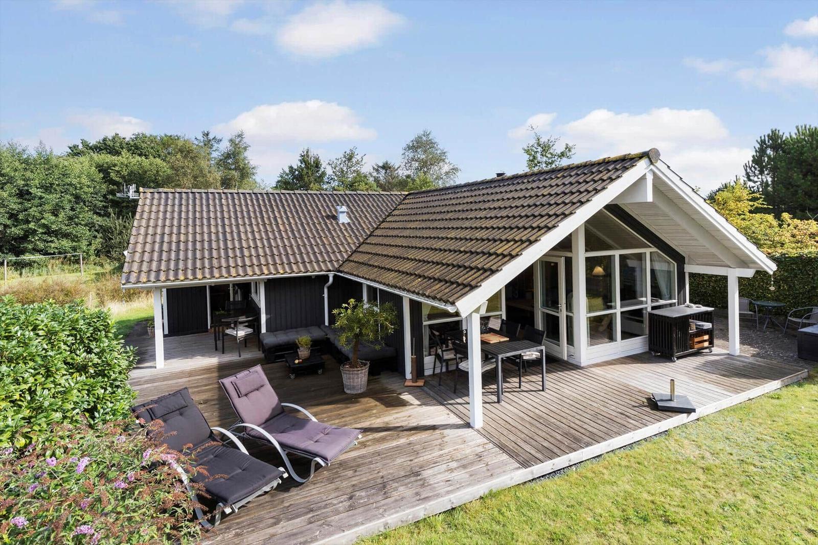 Modern villa with large wooden deck, garden furniture, and view of trees.