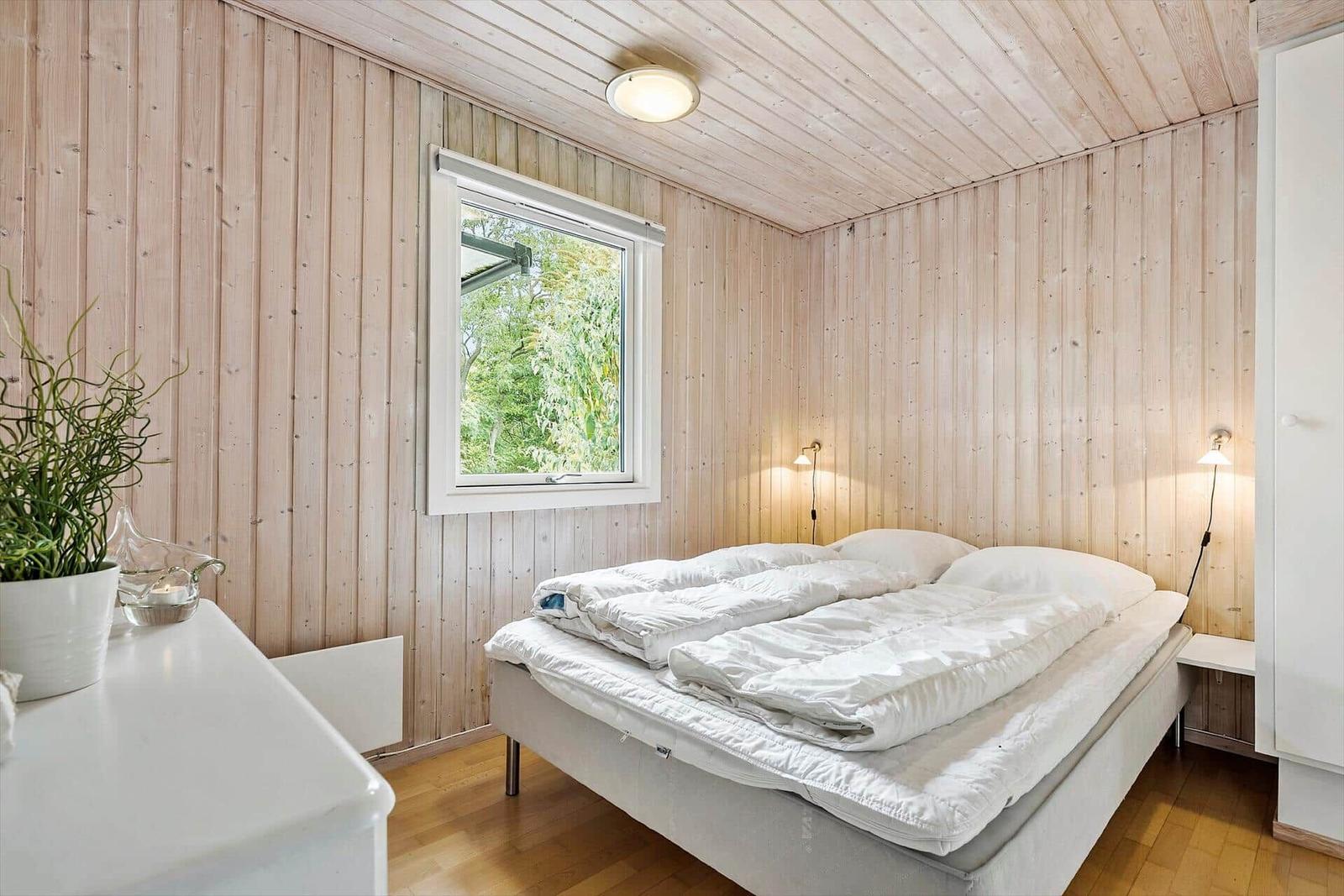 Schlafzimmer mit Holzwänden, Bett und Fenster mit Blick auf Grün.
