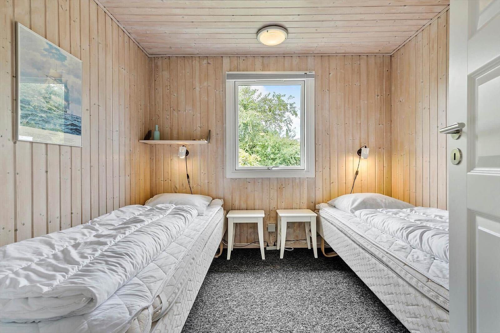 Zwei Schlafplätze mit Matratzen und weißen Bettwäschen. Holzwände, Fenster und kleine Stühle.