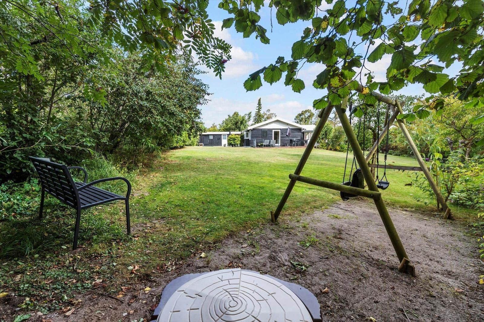 Grüner Garten mit Schaukel, Bank und Haus im Hintergrund.