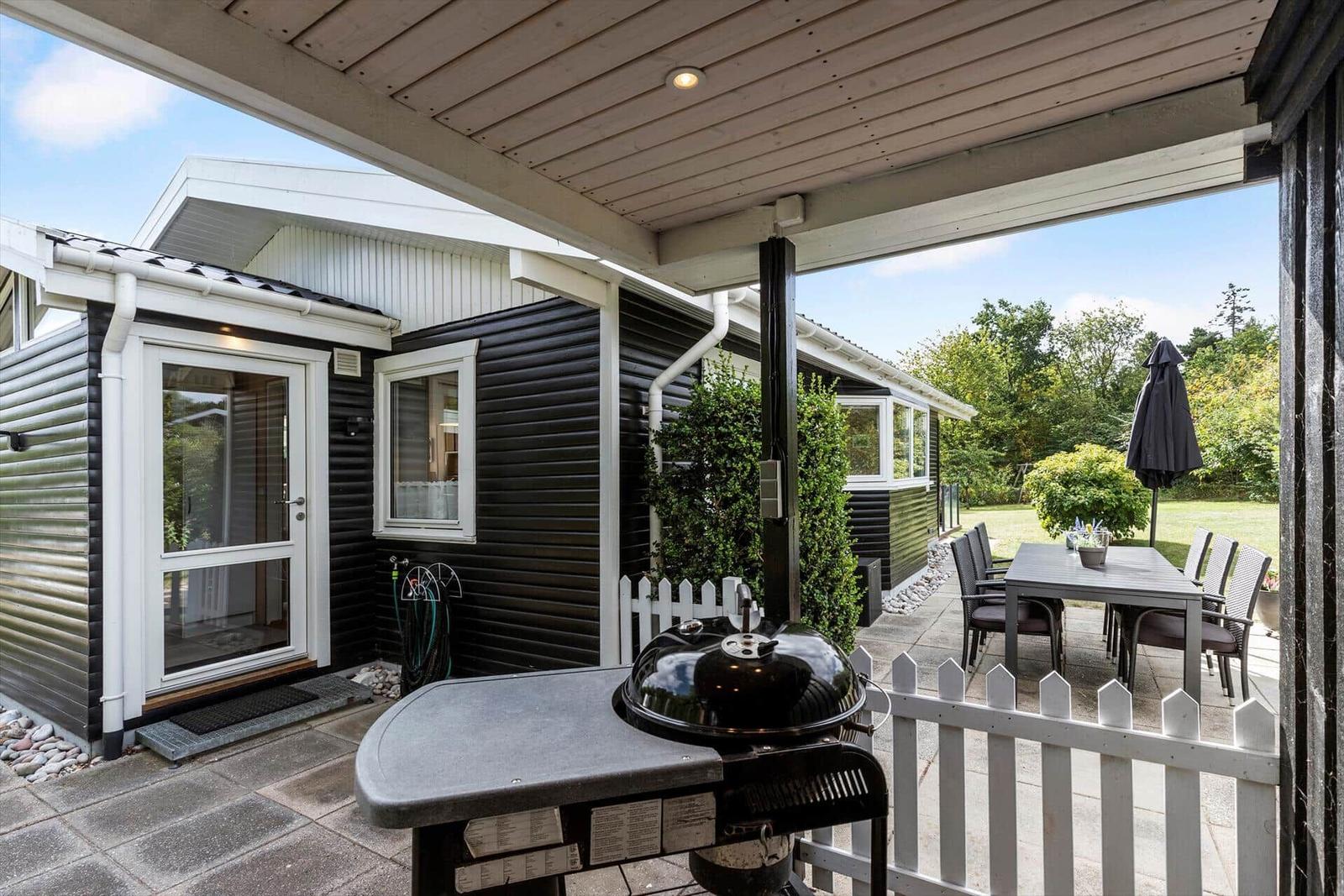 Terrasse mit Grill, Tisch und Stühlen. Hinterhof mit Grünfläche und Gartenmöbeln.