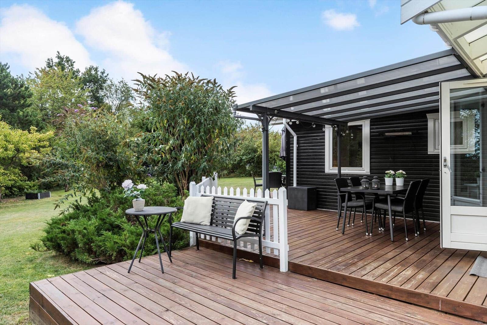 Terrasse mit Sitzgelegenheiten und Gartenbereich. Schwarze Holzwand und Holzdielen.