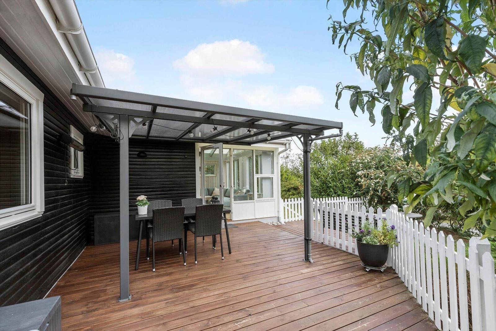 Terrasse mit Sitzgruppe unter Dach, weißer Zaun und Pflanzen