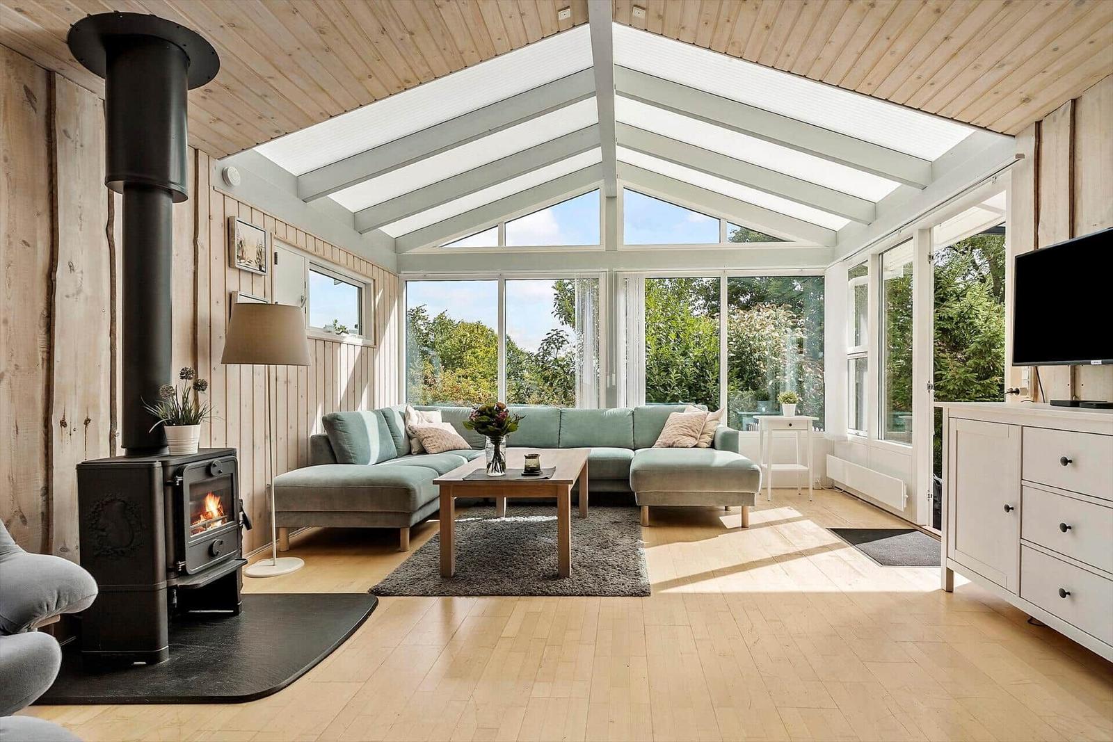 Wohnzimmer mit Holzdecke, Kaminofen und großem Fensterbereich.