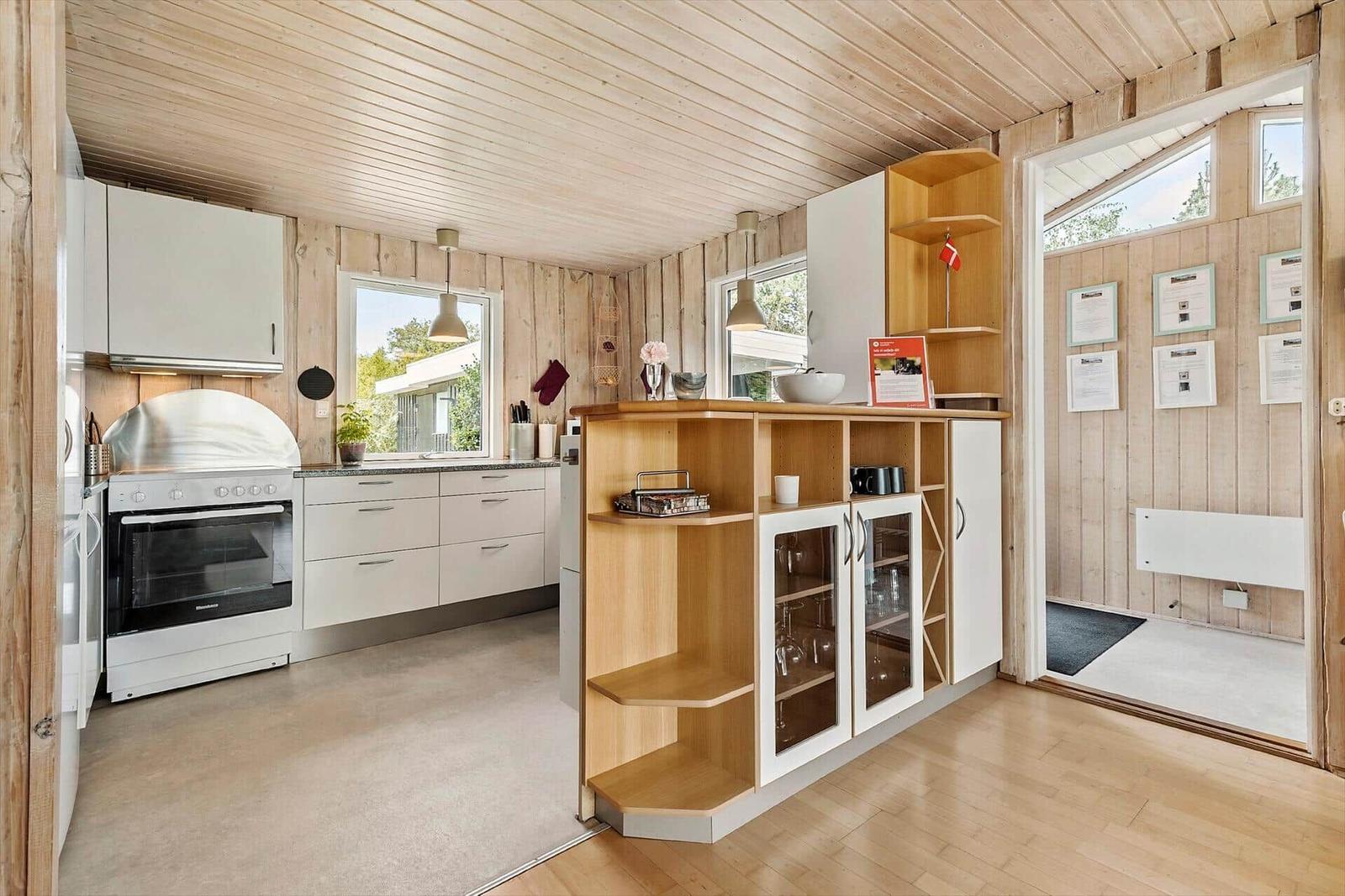 Küche mit Holzwand und weißen Schränken, Kücheninsel mit Glasfront und Fenstern.