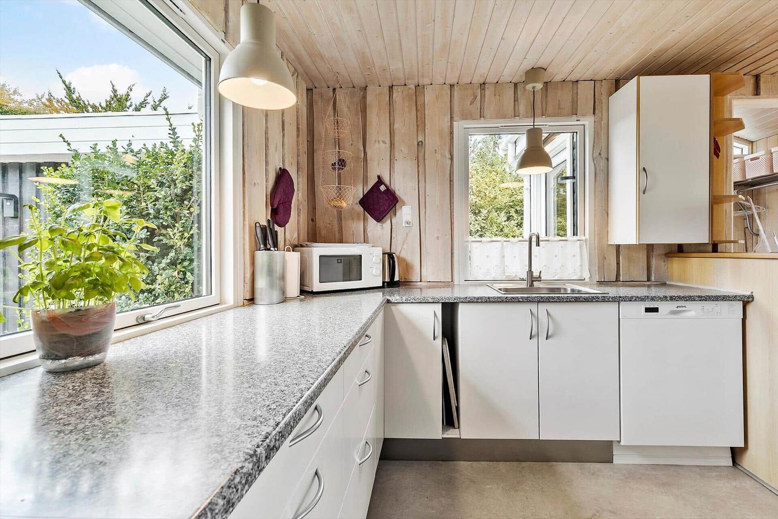 Küche mit Holzwand, Arbeitsplatte und Fenster. Geschirrspüler und Mikrowelle vorhanden.