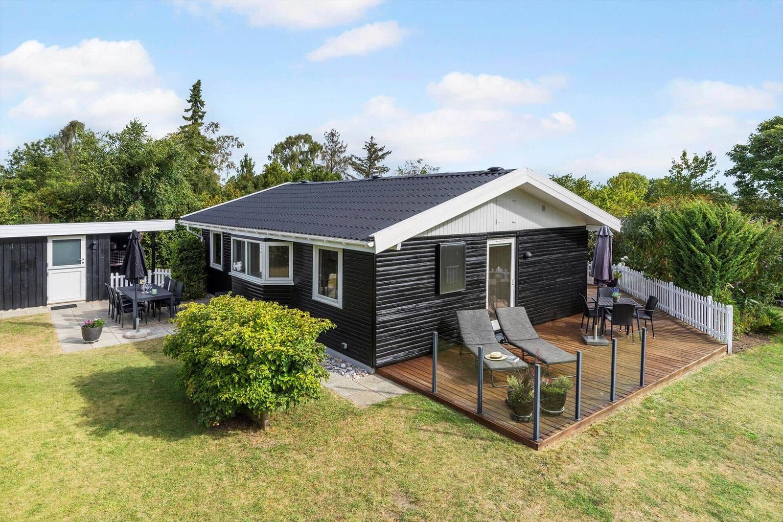 Schwarzes Haus mit Terrasse und Garten. Außengrill, Liegestühle und Tisch sind vorhanden.