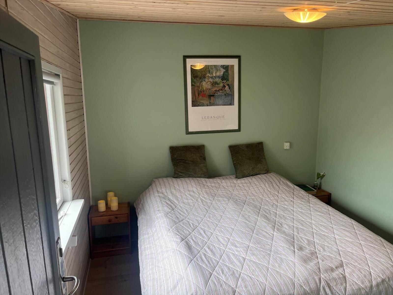 Schlafzimmer mit Bett, Nachttisch und Wandbild. Holzdecke und grüne Wände.