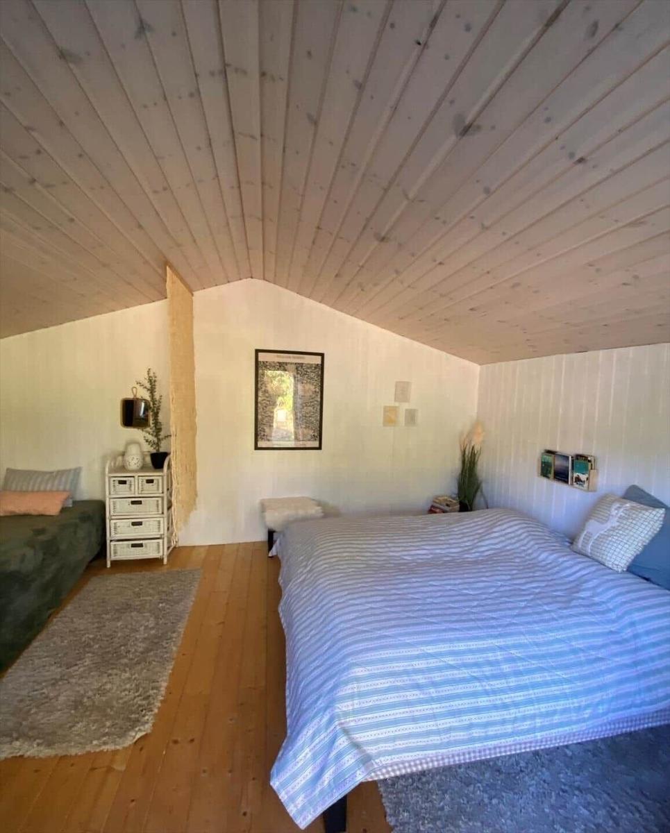 Schlafzimmer mit Dachschrägen, Bett und kleinem Sofa. Holzfußboden und weiße Wände.