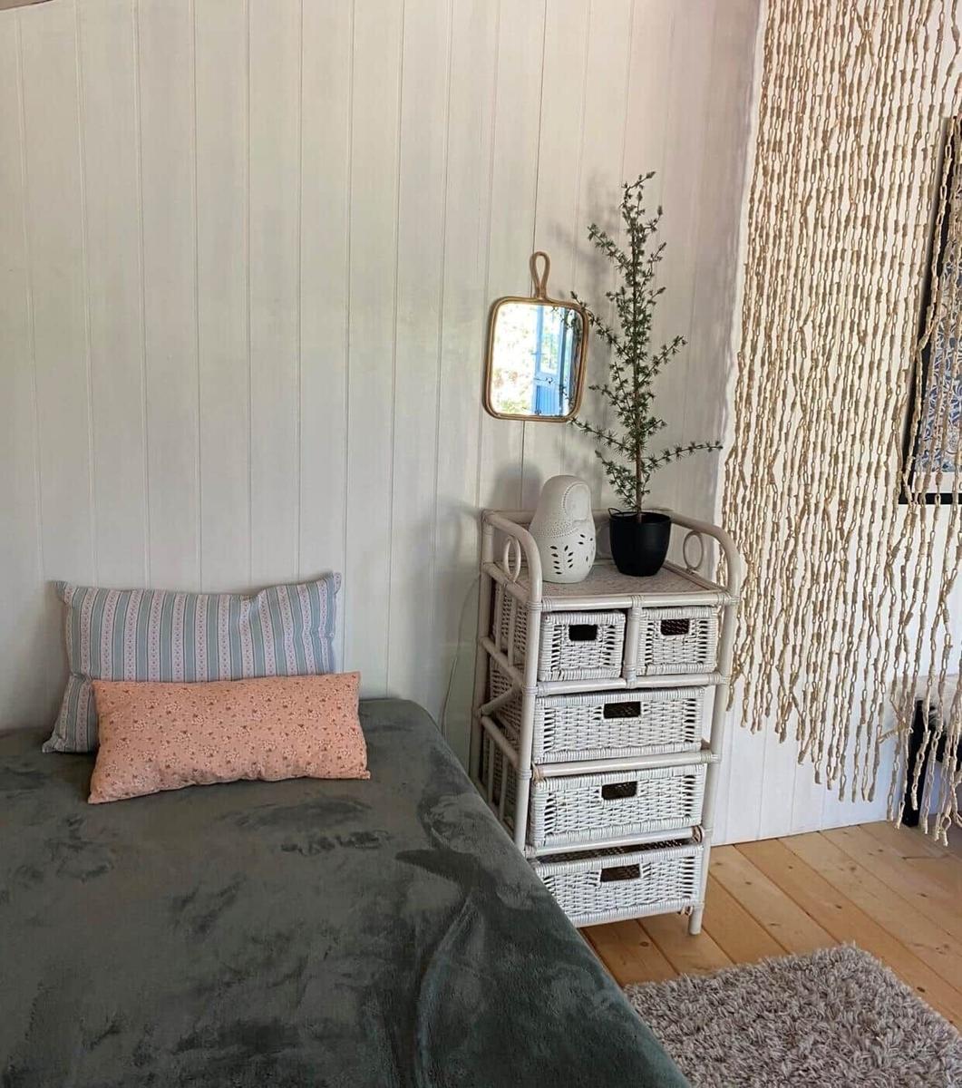 Ein Bett mit Kissen und einem Korbregal an der Wand.